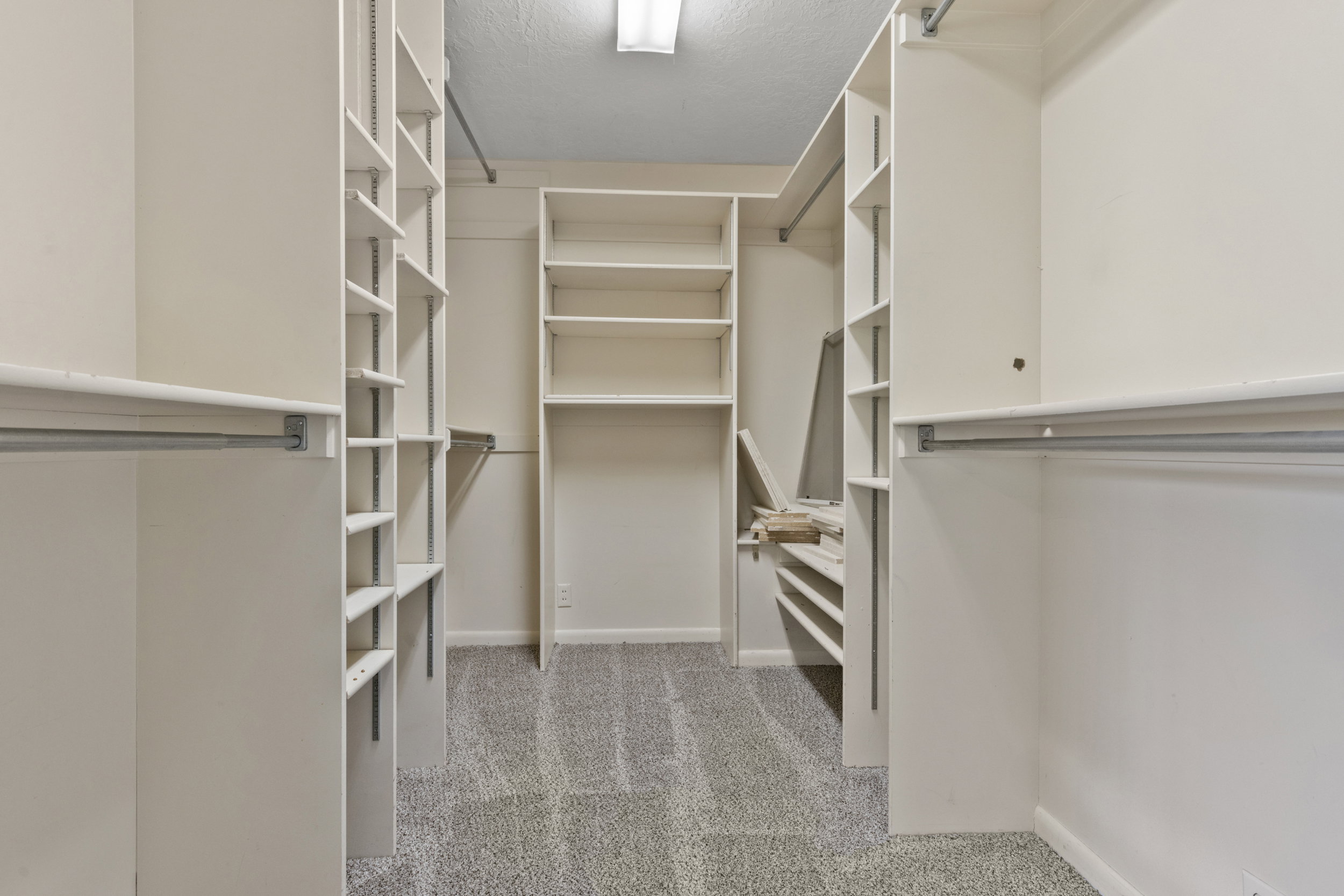 Walk-in closet featuring extensive built-in shelving, multiple hanging rods, and light-colored carpeting