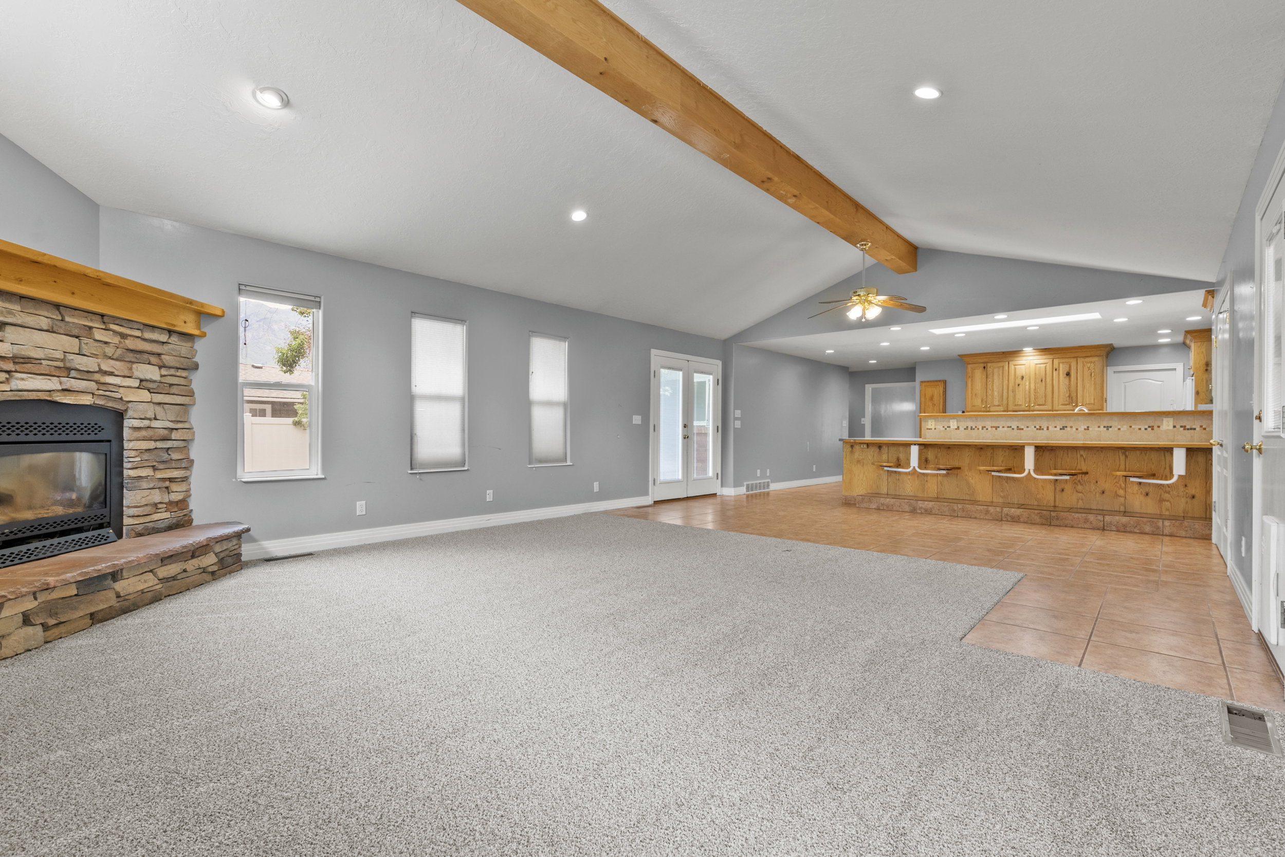 Spacious living area featuring a stone-faced fireplace with a wood mantle, vaulted ceilings with exposed beams, and light gray wall tones