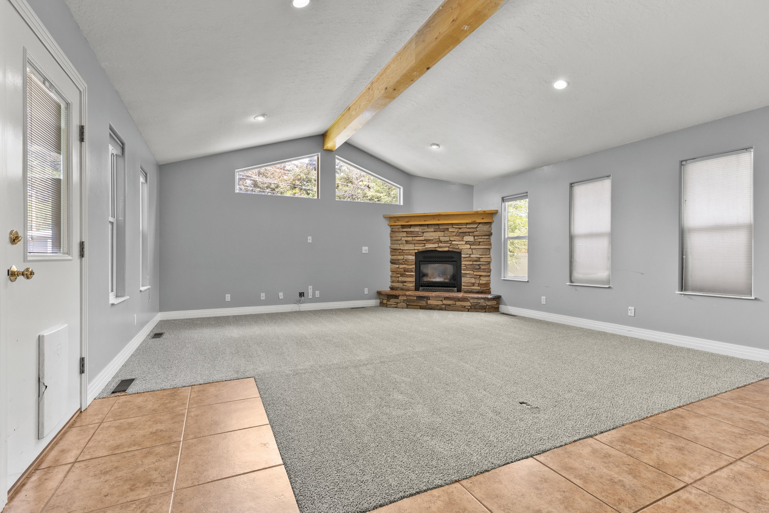 Spacious living area featuring a stone fireplace with a wood mantel, vaulted ceiling with exposed wood beam, recessed lighting, and multiple windows