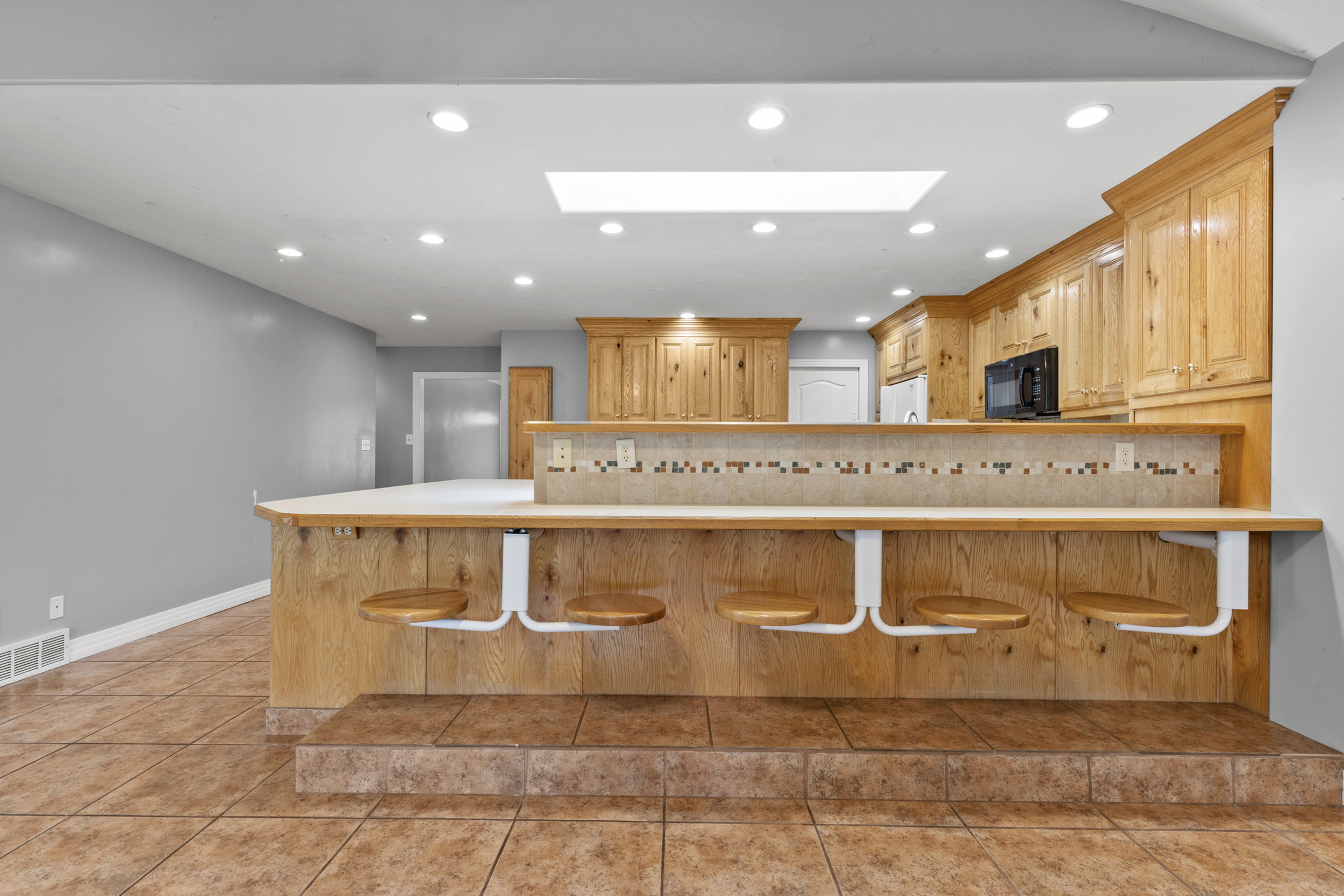 Kitchen island featuring a tiled bar-height counter with built-in seating, wood cabinetry, recessed lighting, and a skylight