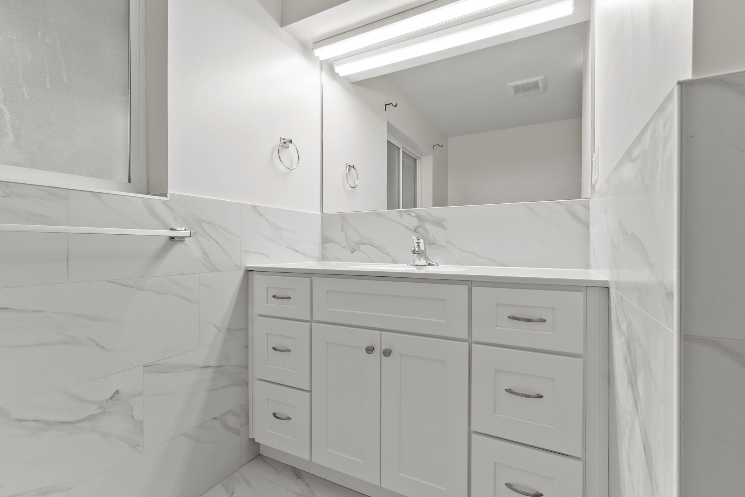 Vanity with white shaker-style cabinetry, a white countertop, and a chrome faucet