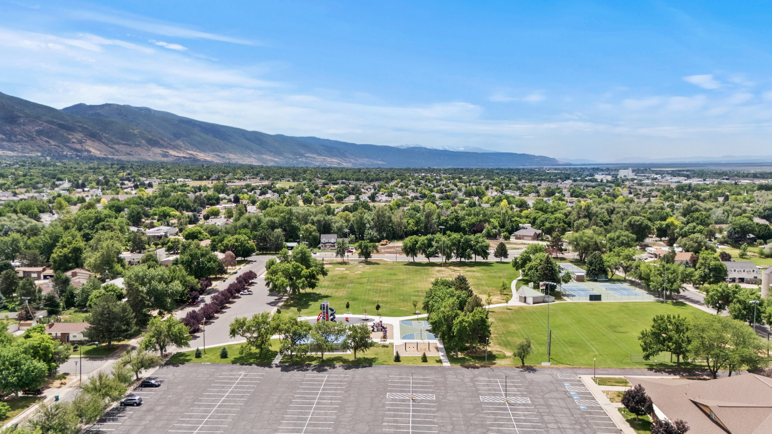Expansive park grounds featuring a large grassy area, mature trees, and a tennis court