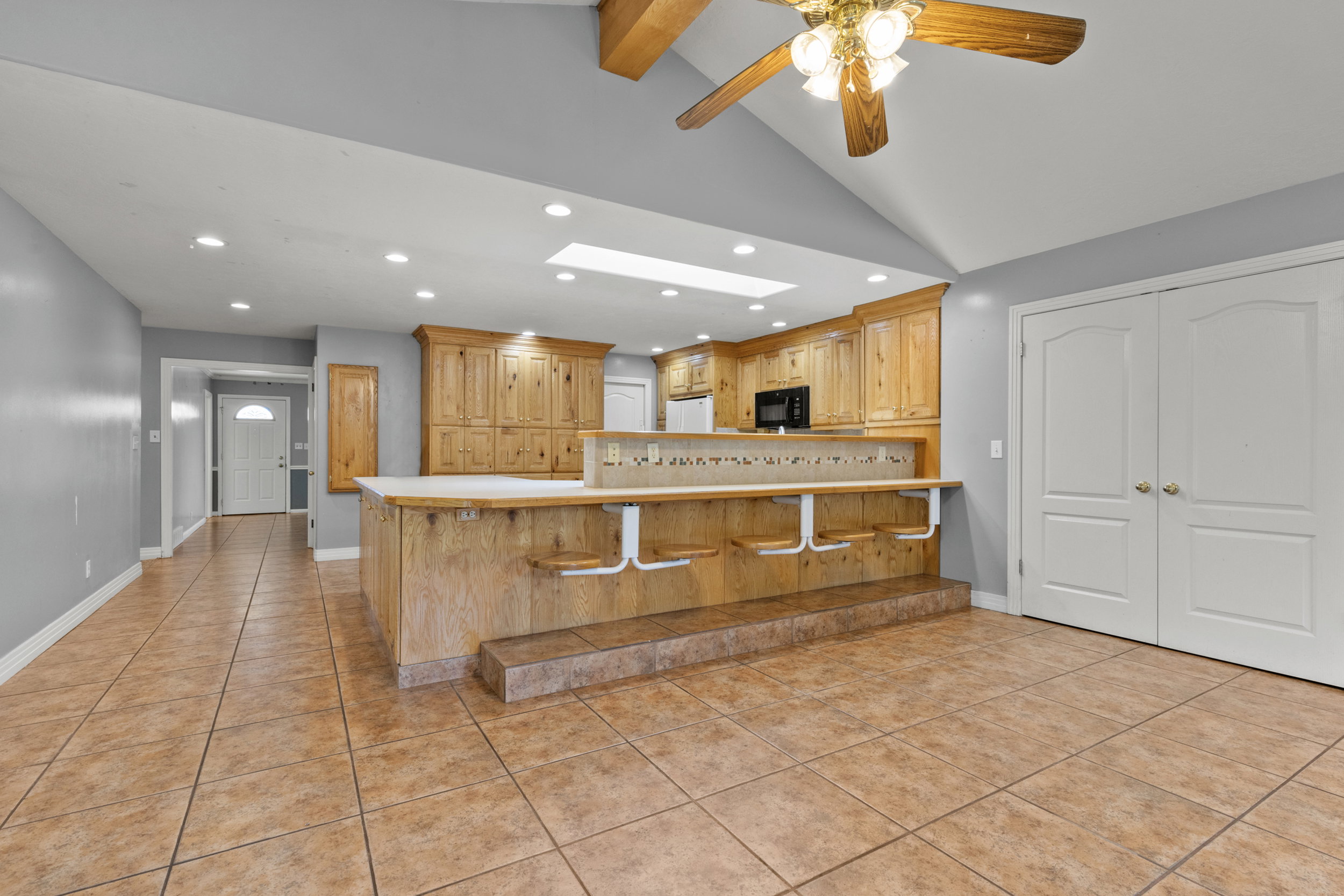 Open-concept living area featuring terracotta-style tile flooring, vaulted ceilings, and a wood-finish ceiling fan