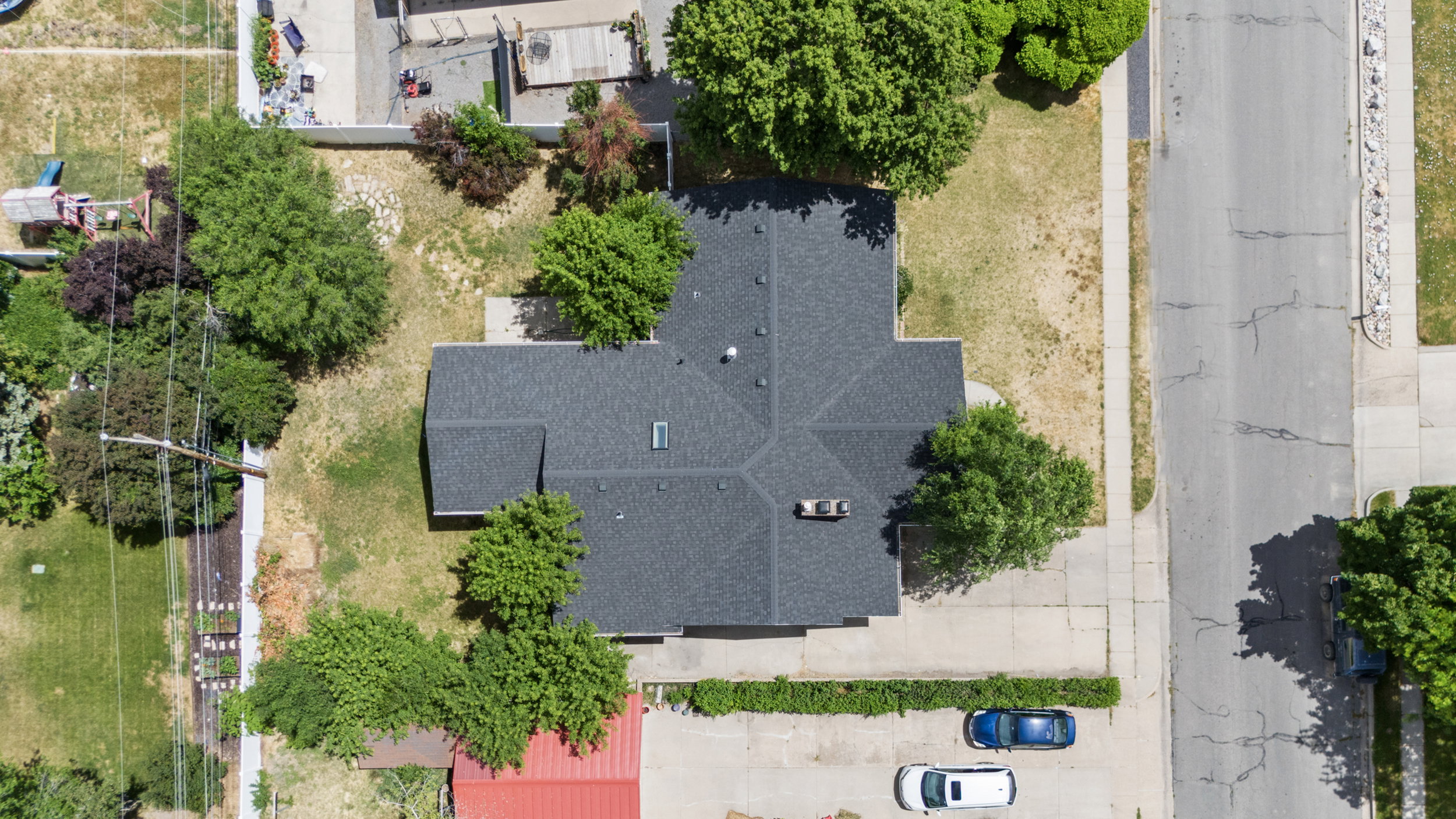 Property featuring a dark shingle roof with a skylight, surrounded by mature trees and a substantial land area