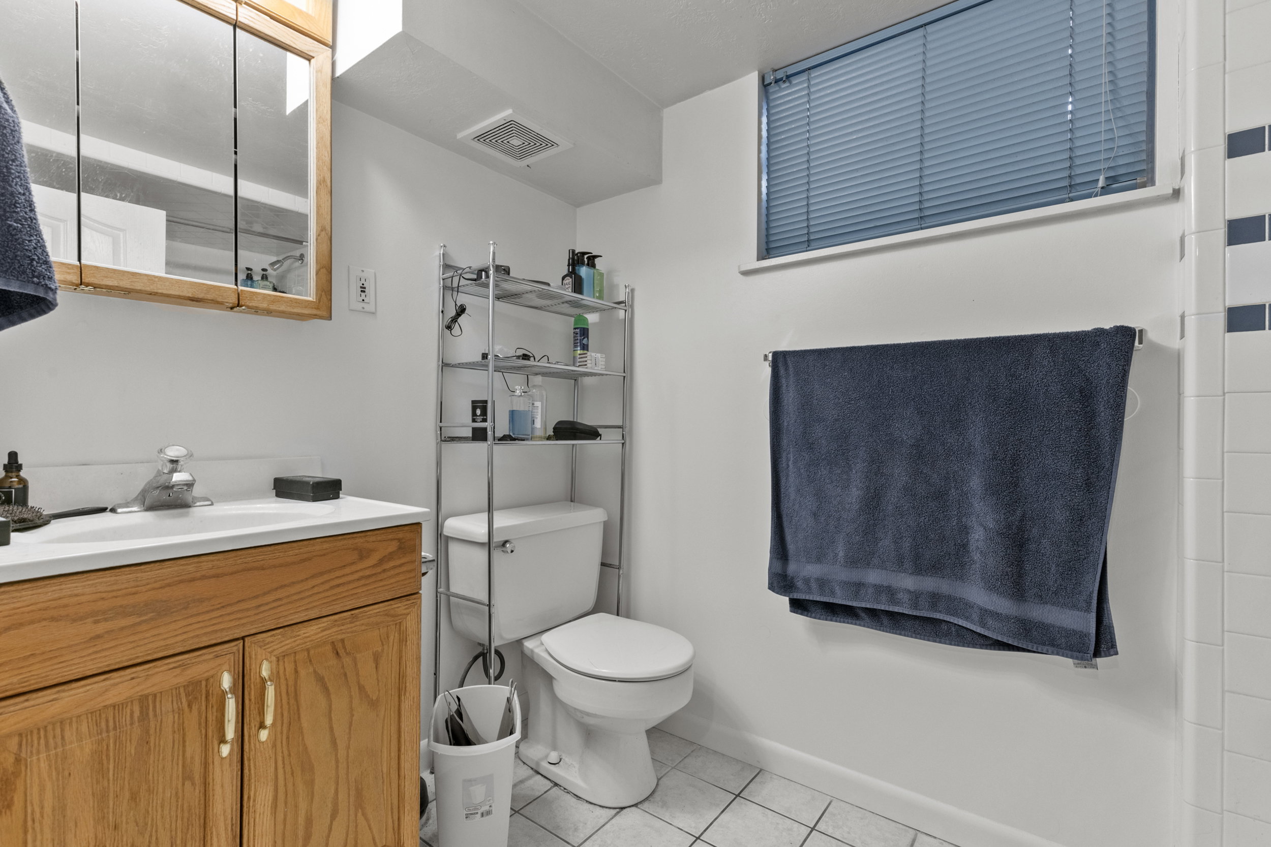 Bathroom featuring a wood vanity with a white countertop, wall-mounted medicine cabinet, white tiled flooring, and a white toilet