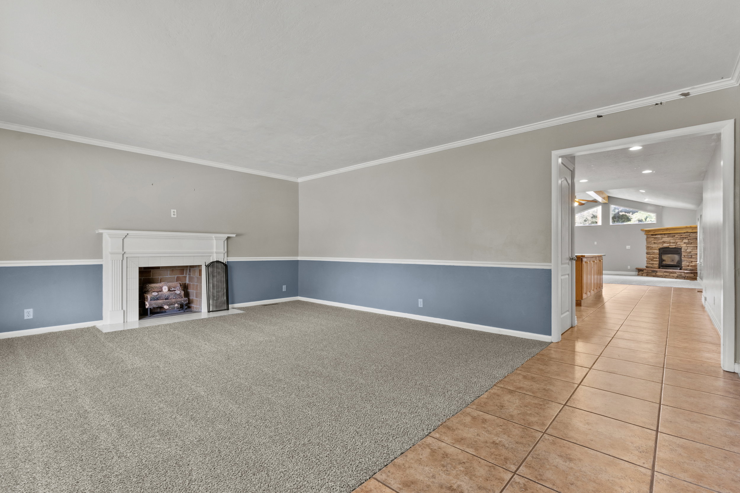 Spacious room featuring a white fireplace mantel, brick firebox, and neutral carpet flooring