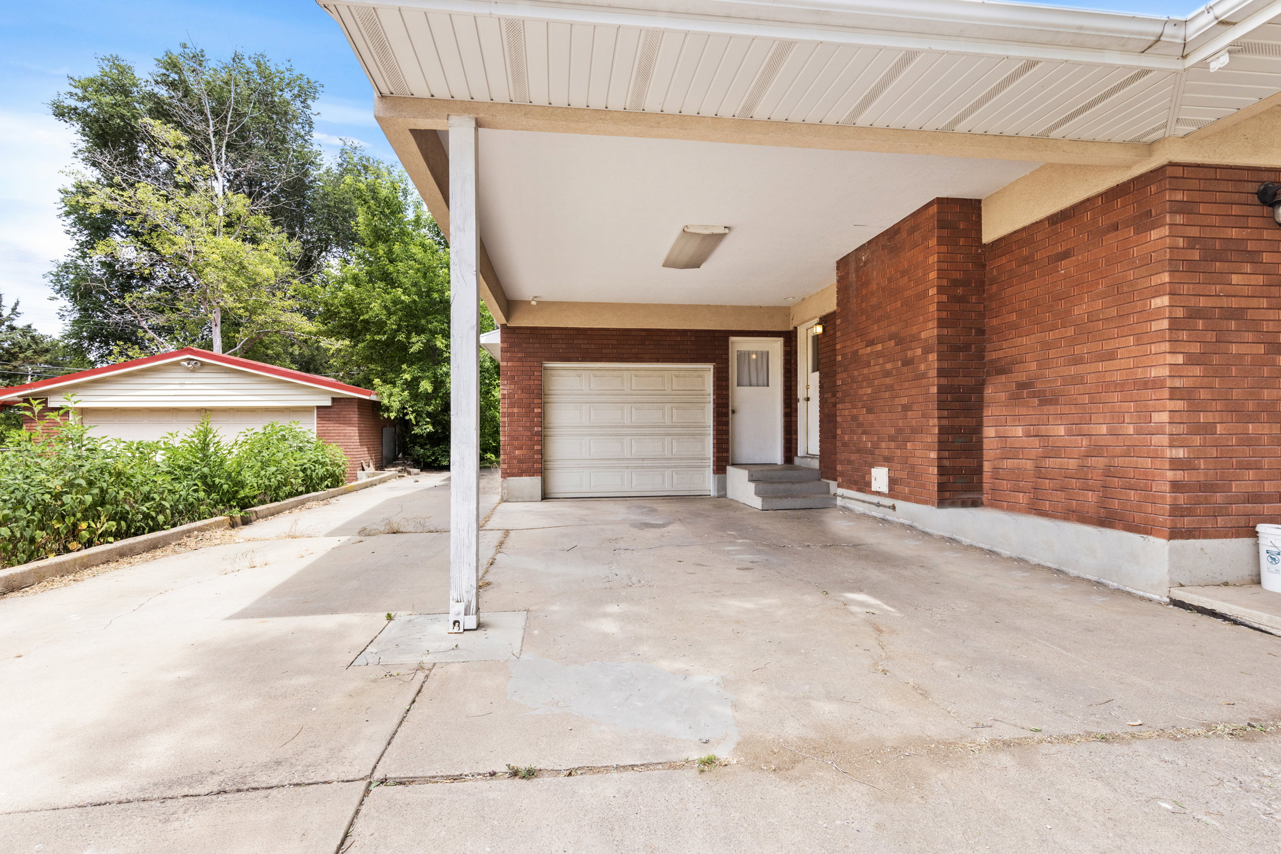 Covered carport with concrete flooring, red brick exterior, and attached garage with a white door