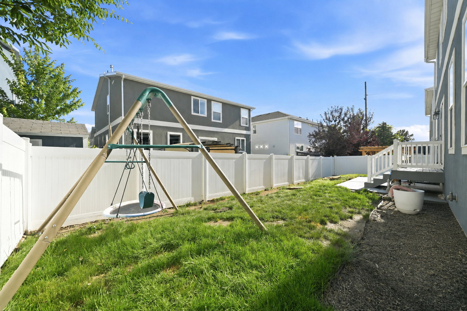 Expansive backyard featuring a green lawn, white vinyl fencing, and a built-in deck with railings