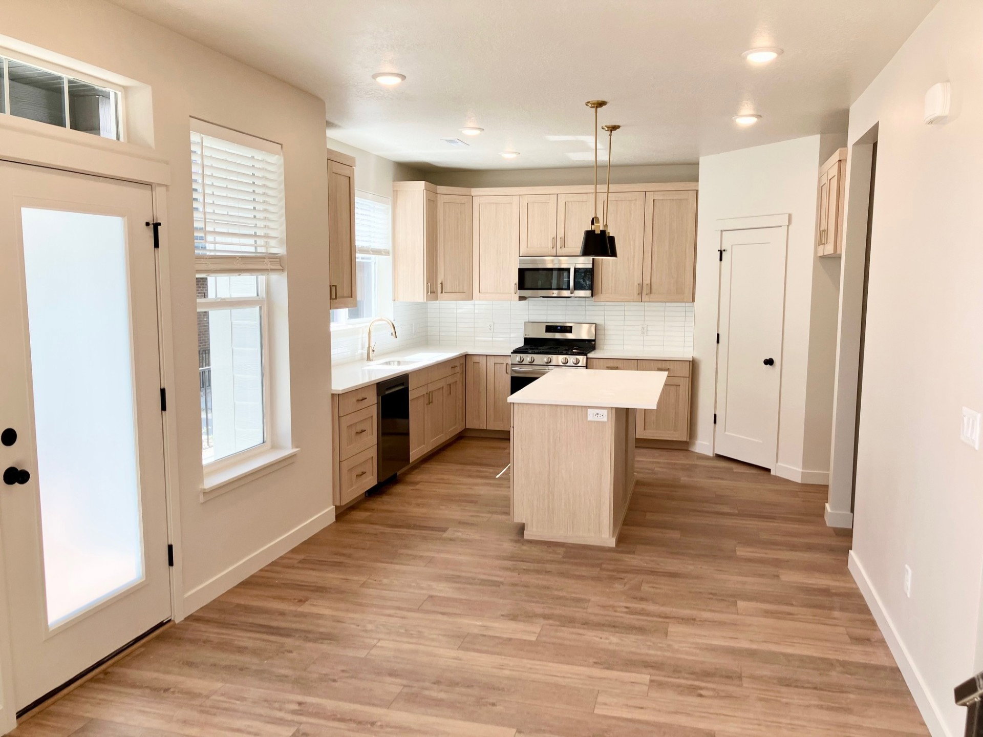Open-concept kitchen featuring wood-finish flooring, light wood cabinetry, white subway tile backsplash, and stainless steel appliances