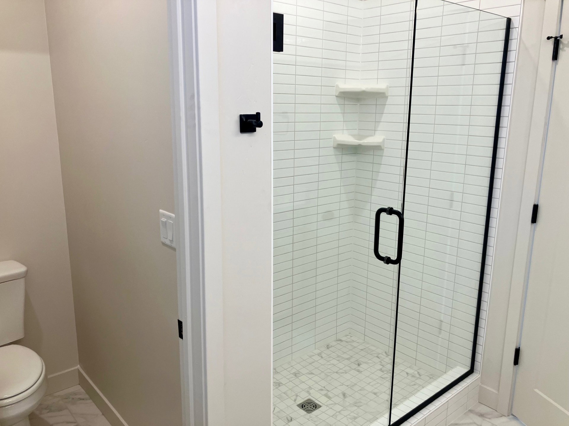 Spacious glass-enclosed shower featuring white subway tile, a marble-patterned base, and matte black hardware