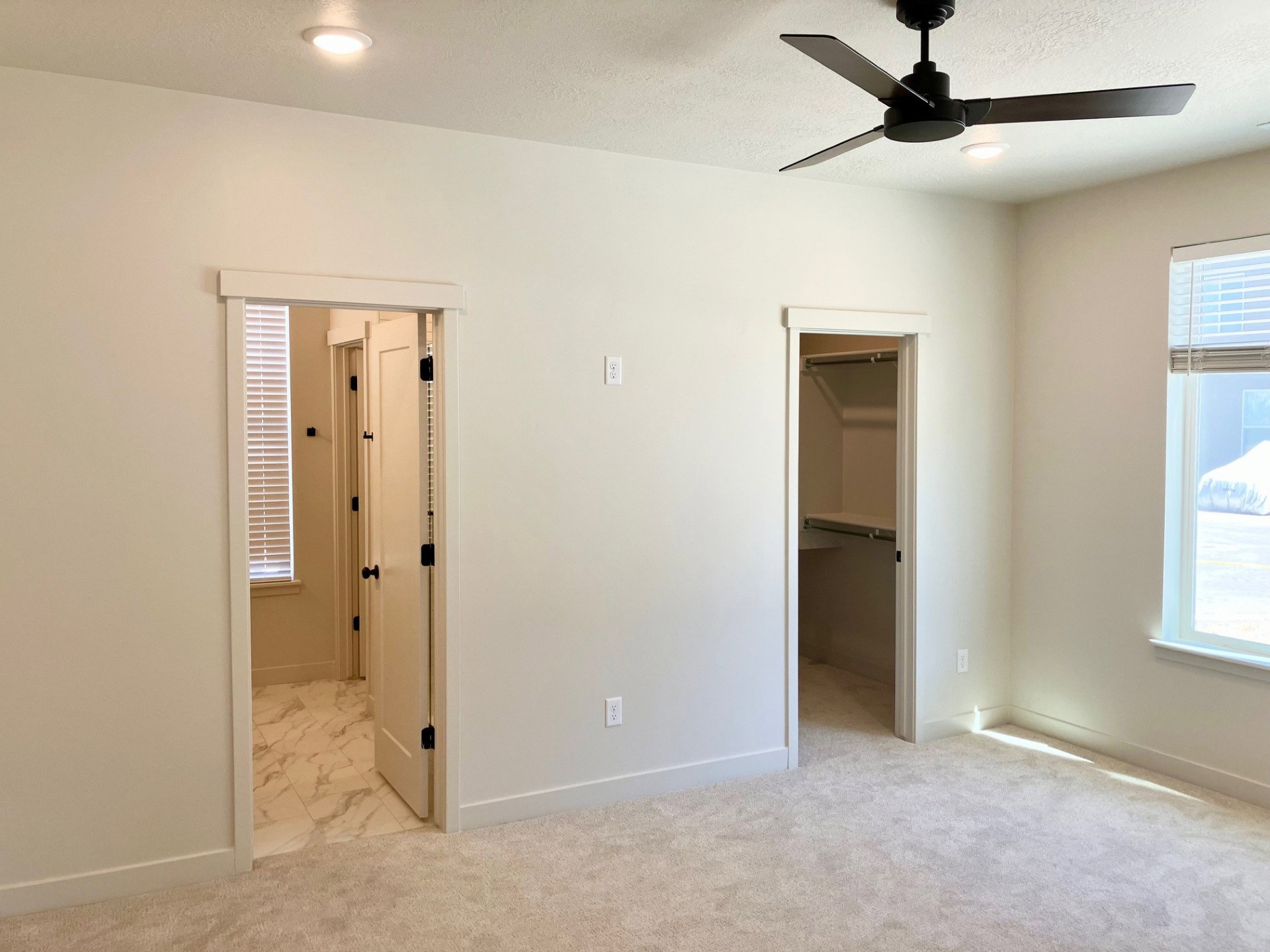 Carpeted interior space featuring a matte black ceiling fan with integrated lighting, recessed ceiling lights, and two doorways with white trim