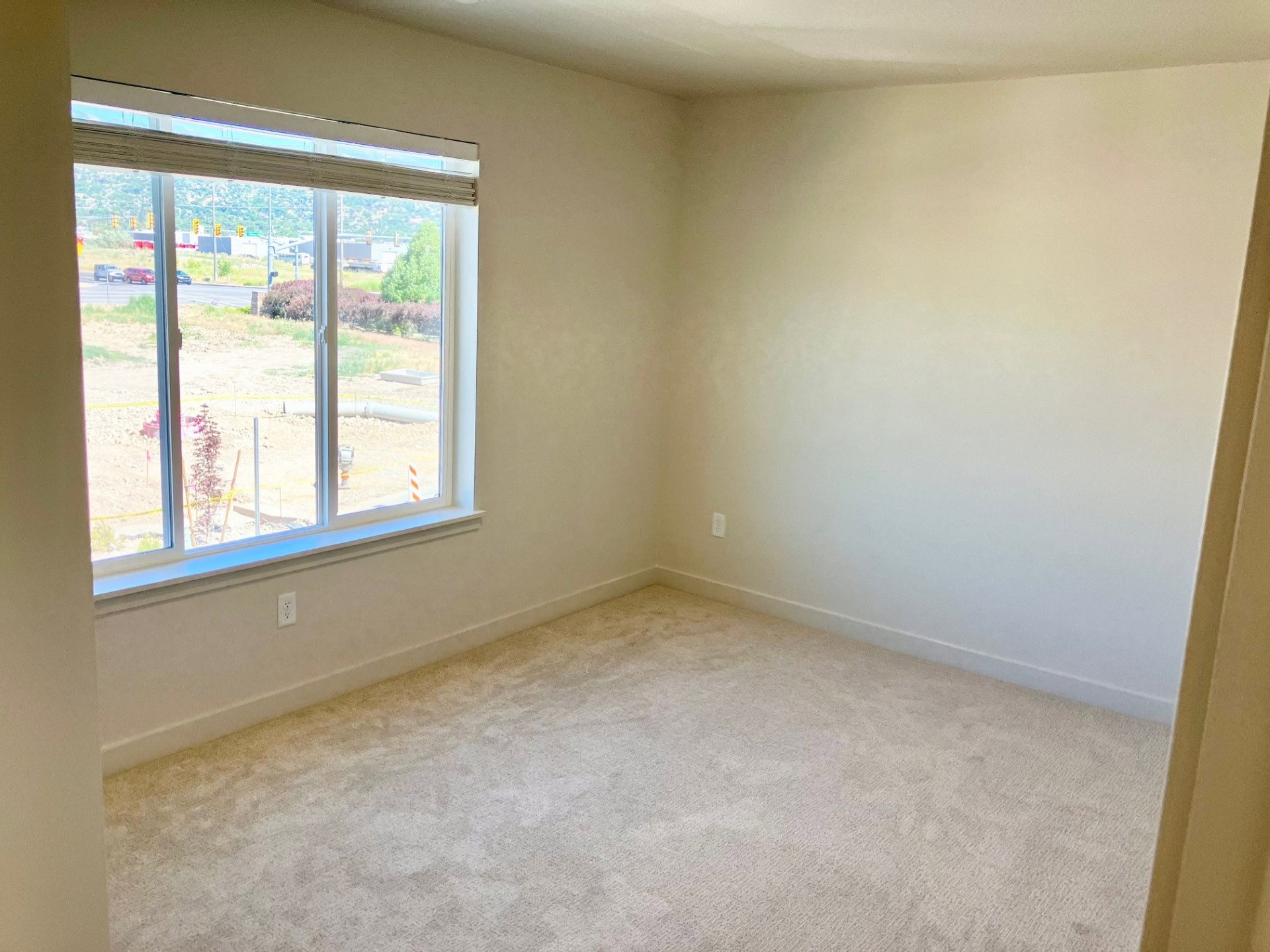 Neutral tone walls and light-colored carpeting define this room, featuring a large window with horizontal blinds