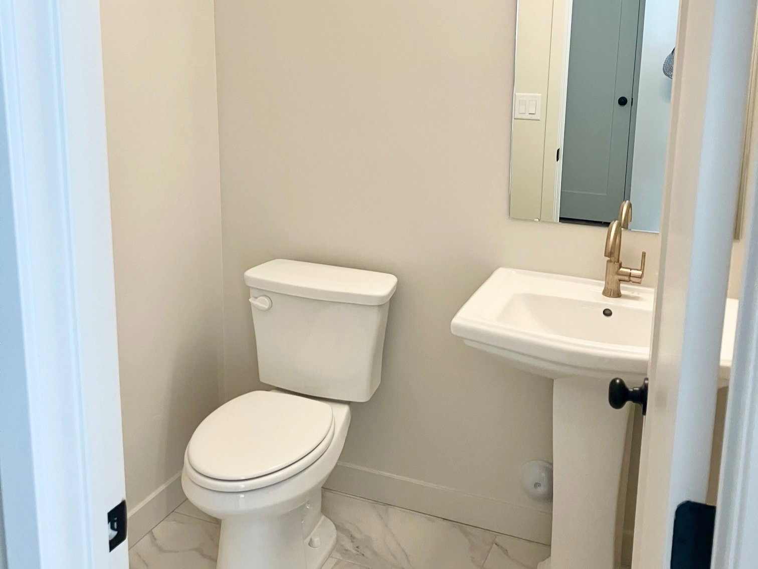 White pedestal sink with a gold-finish faucet, rectangular mirror, and a linear vanity light fixture