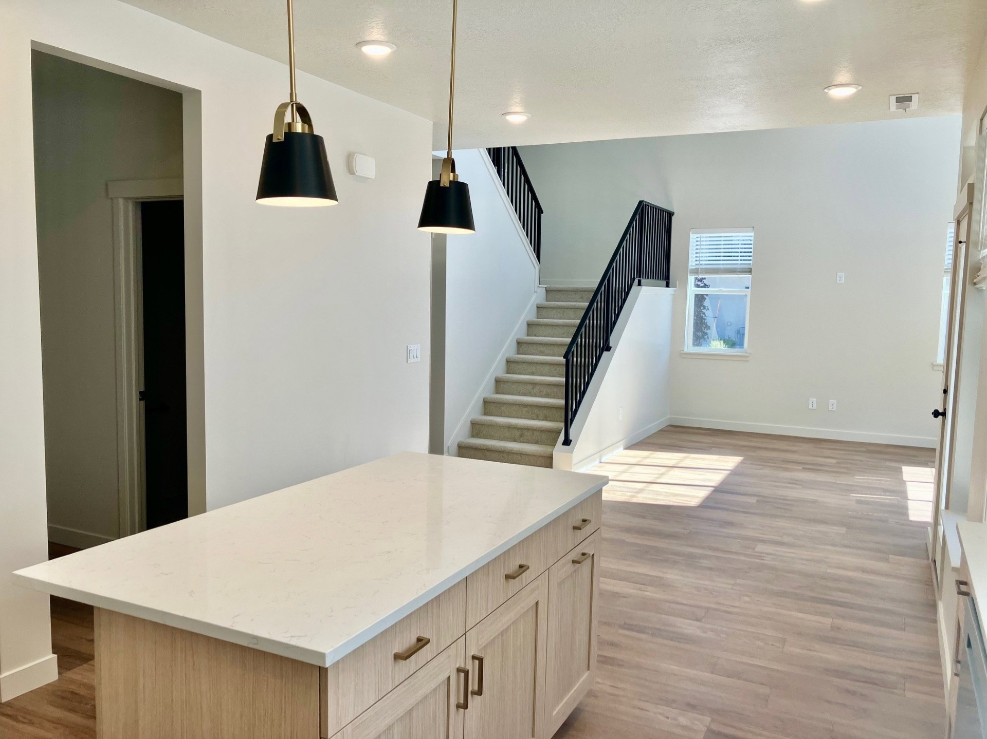 Kitchen island with a light-toned countertop and cabinetry, illuminated by two modern black and brass pendant lights