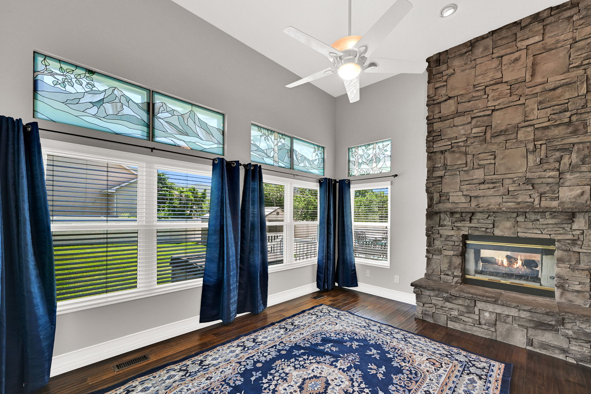 Spacious living area featuring a floor-to-ceiling stone fireplace, high vaulted ceilings, and dark wood-finish flooring