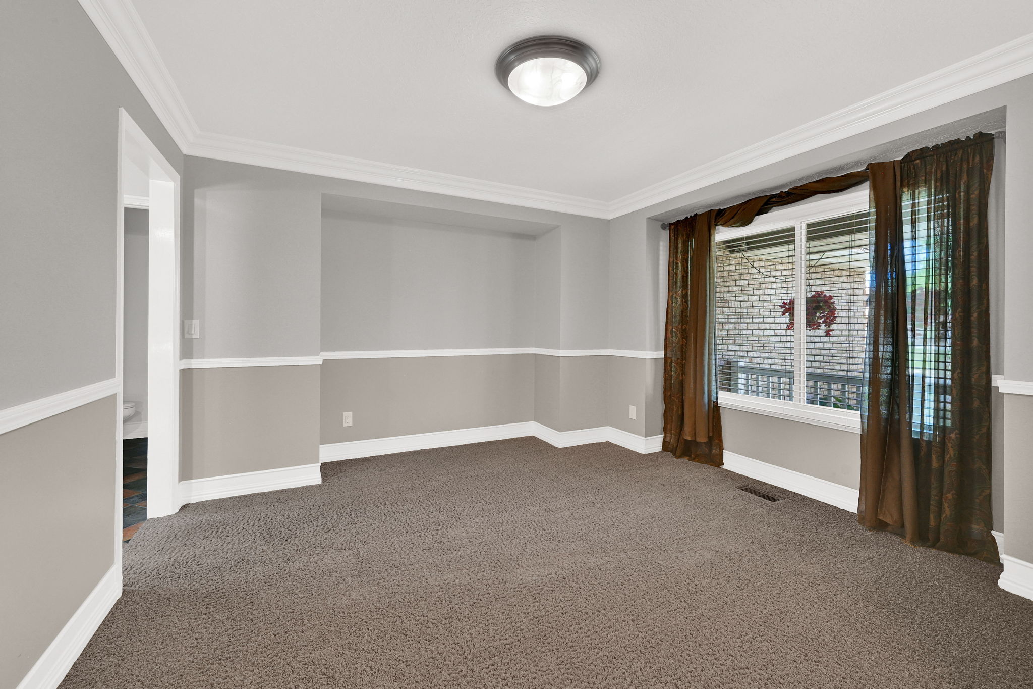 Carpeted room featuring a large window with white trim, two-tone painted walls, white crown molding, and a flush-mount ceiling light fixture