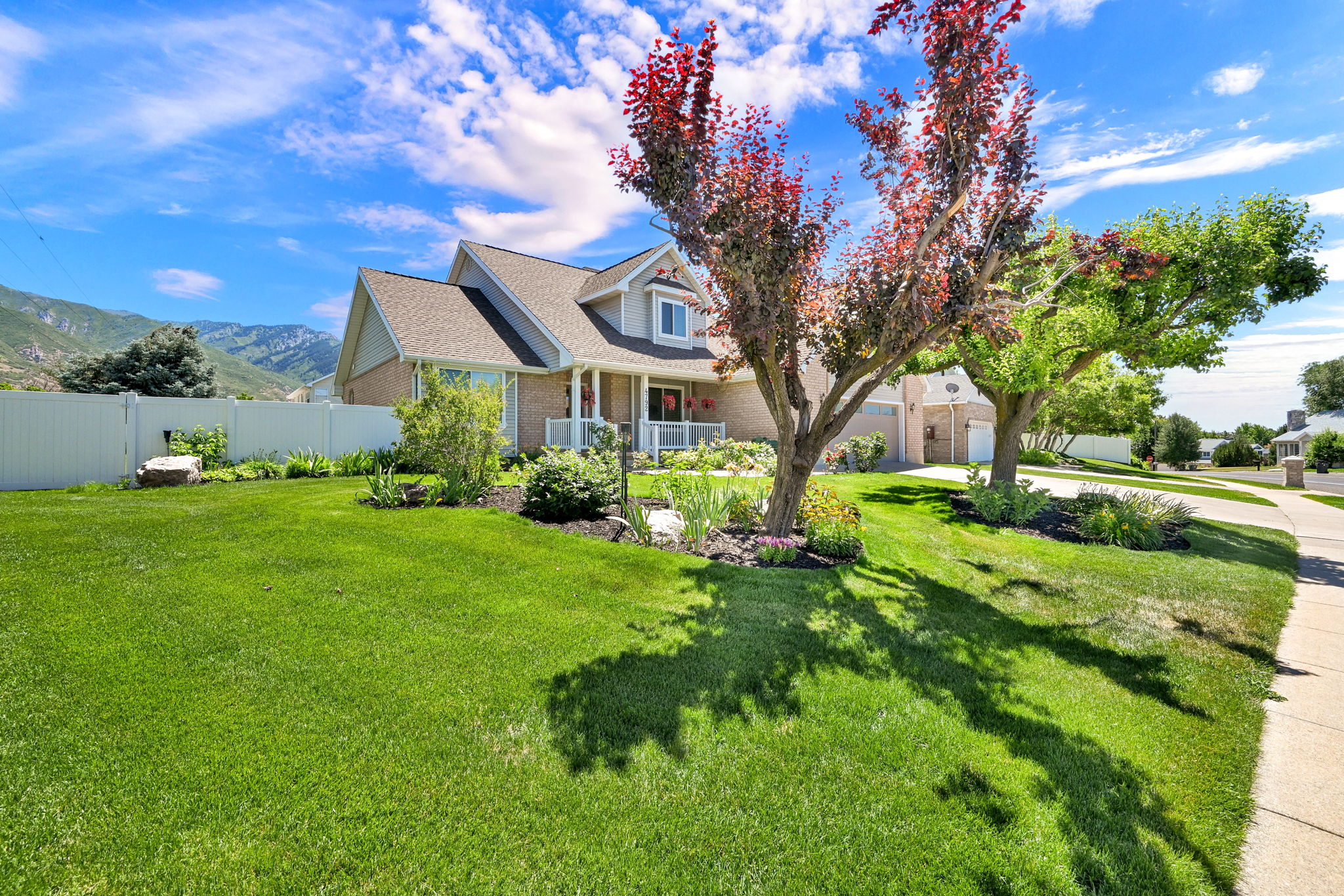 Expansive front lawn with mature trees and established landscaping beds with vehicle access to back yard through gate on left
