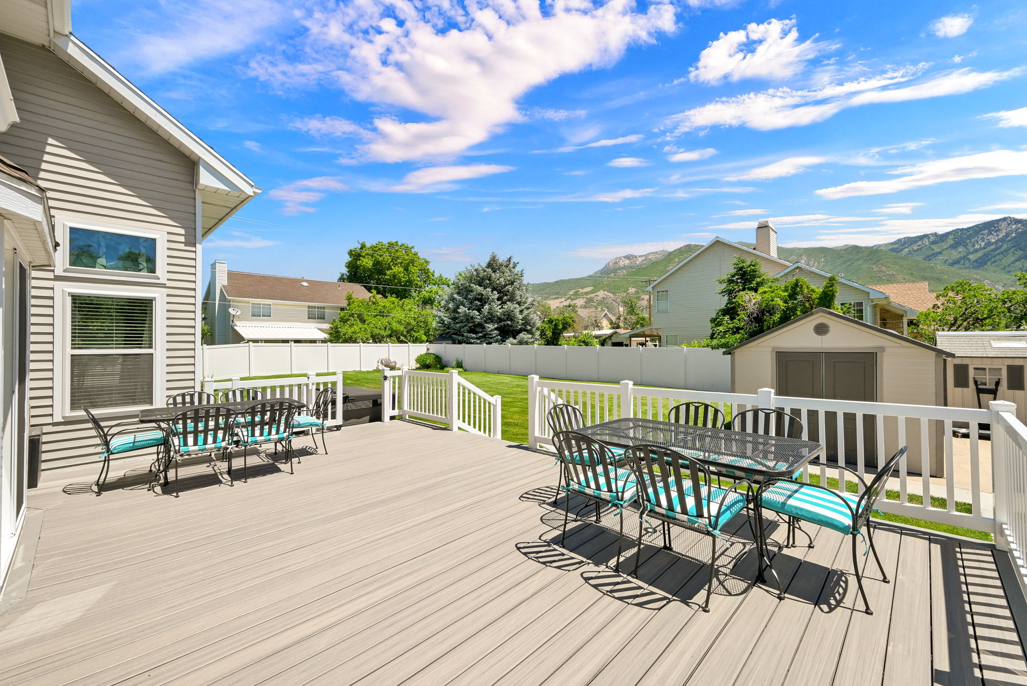 Spacious composite deck with white railing overlooking a fenced backyard featuring a manicured lawn and mature trees