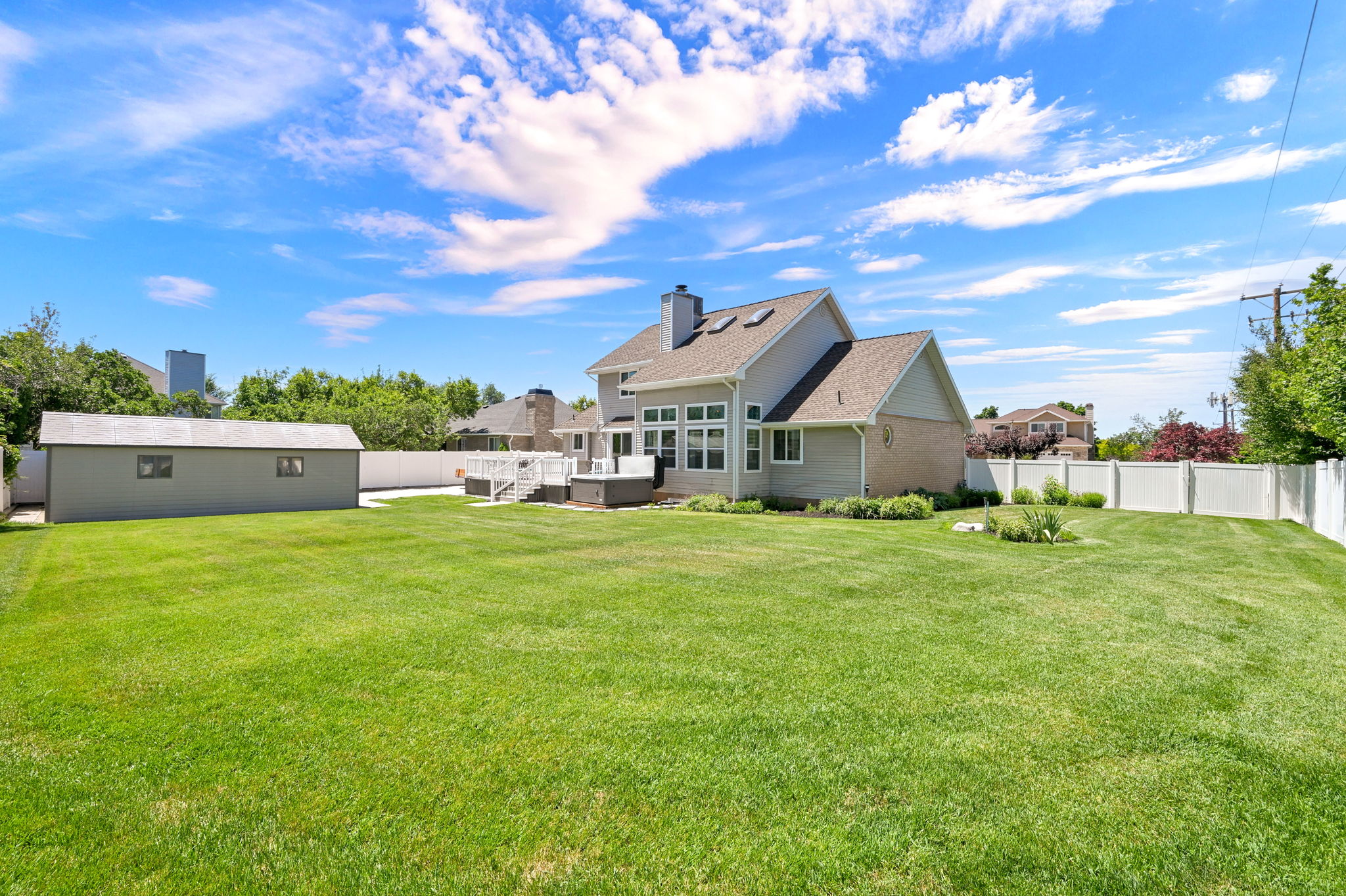 Expansive green lawn bordering a light-sided home with large deck and second drive through gate on the north side of property