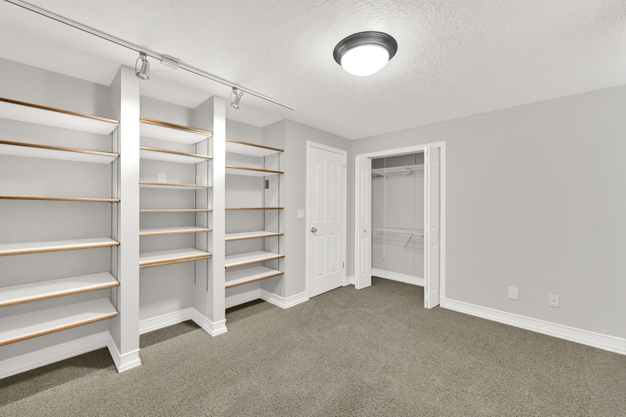 Bedroom #5 (or office) featuring built-in shelving with wood-finish accents, track lighting, and neutral carpeting
