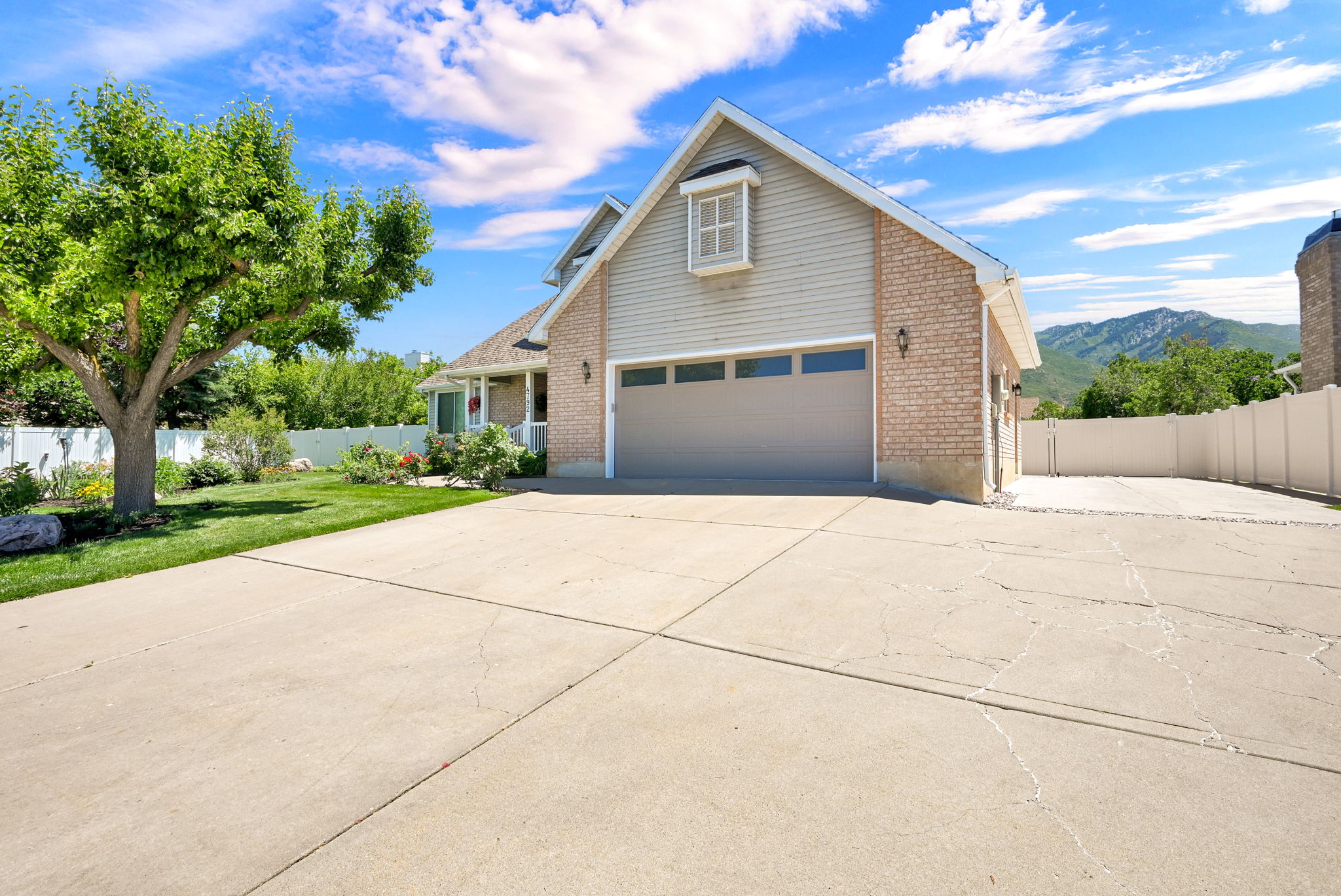 Light brick and siding exterior featuring a multi-car driveway, attached garage, manicured lawn, and mature tree