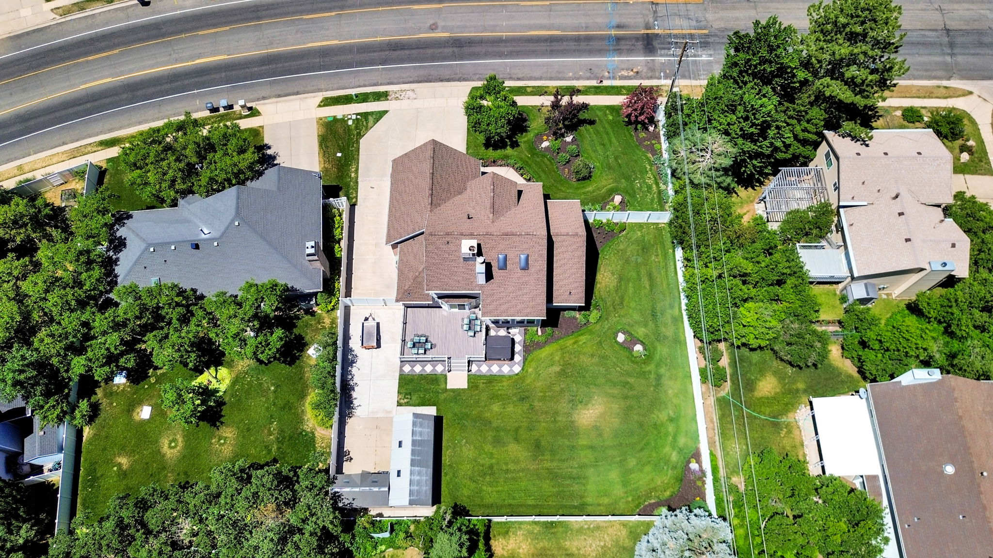 Aerial perspective showcasing a property with a spacious, green lawn, an expansive concrete driveway, and a large deck