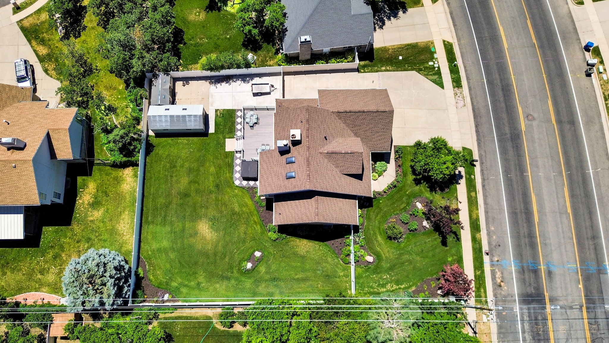Expansive residential property featuring a large green lawn, a deck, a detached sheds, a concrete patio, and mature landscaping