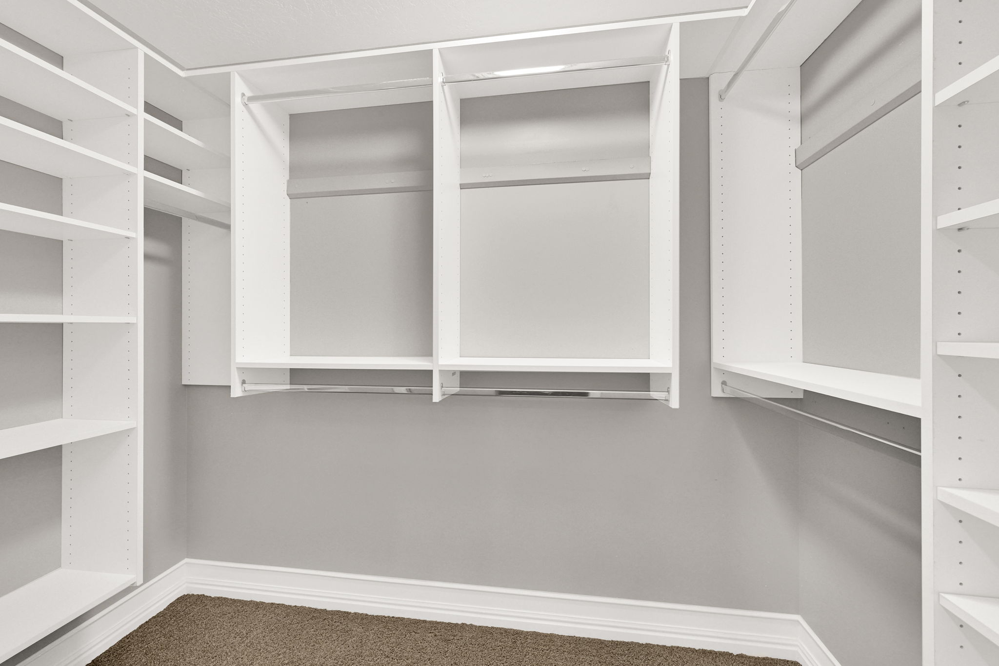Primary suite walk-in closet featuring white built-in shelving, multiple hanging rods, and carpeting