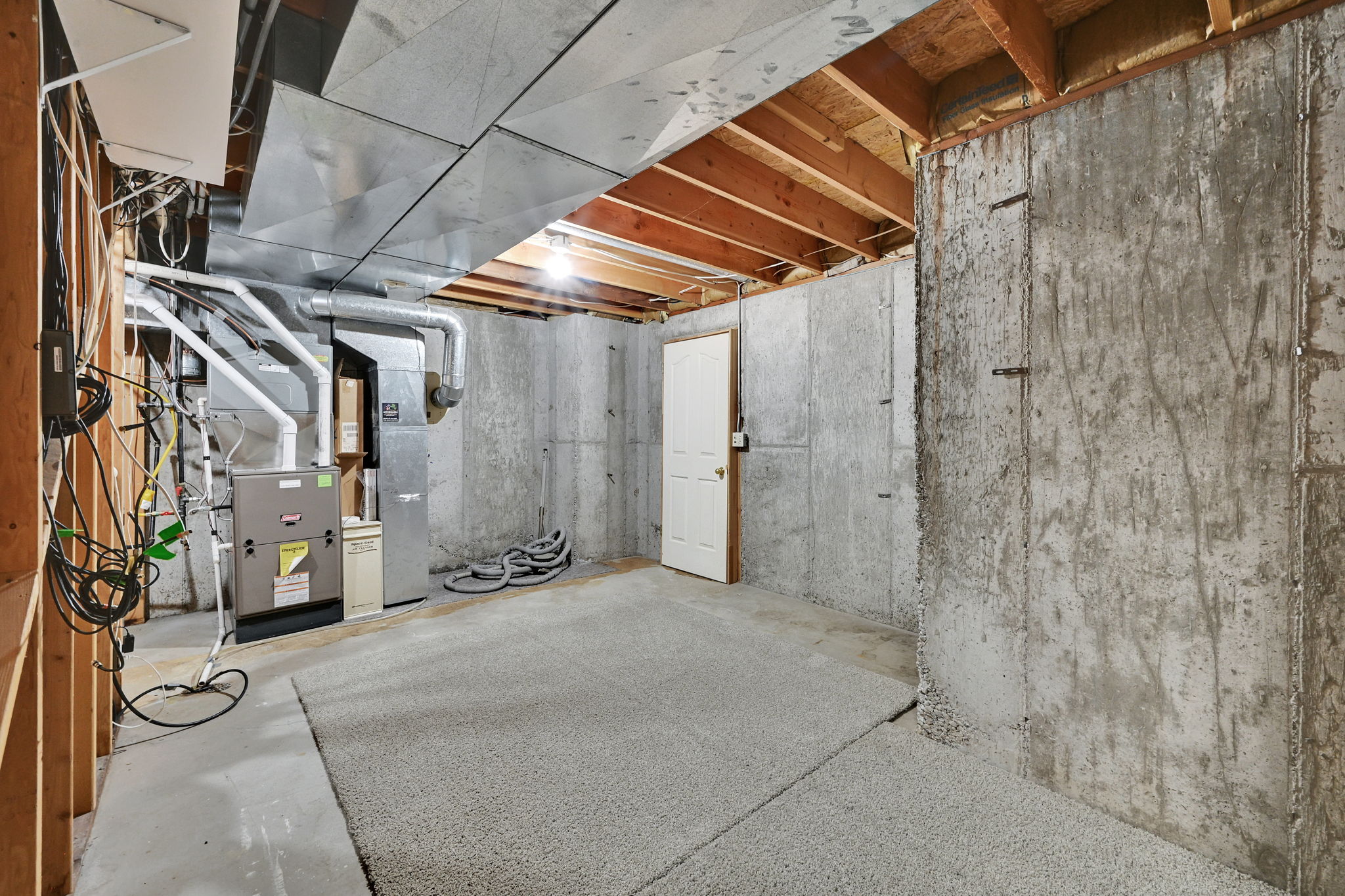 Large unfinished utility room with access to under front porch storage featuring exposed concrete walls and ceiling joists