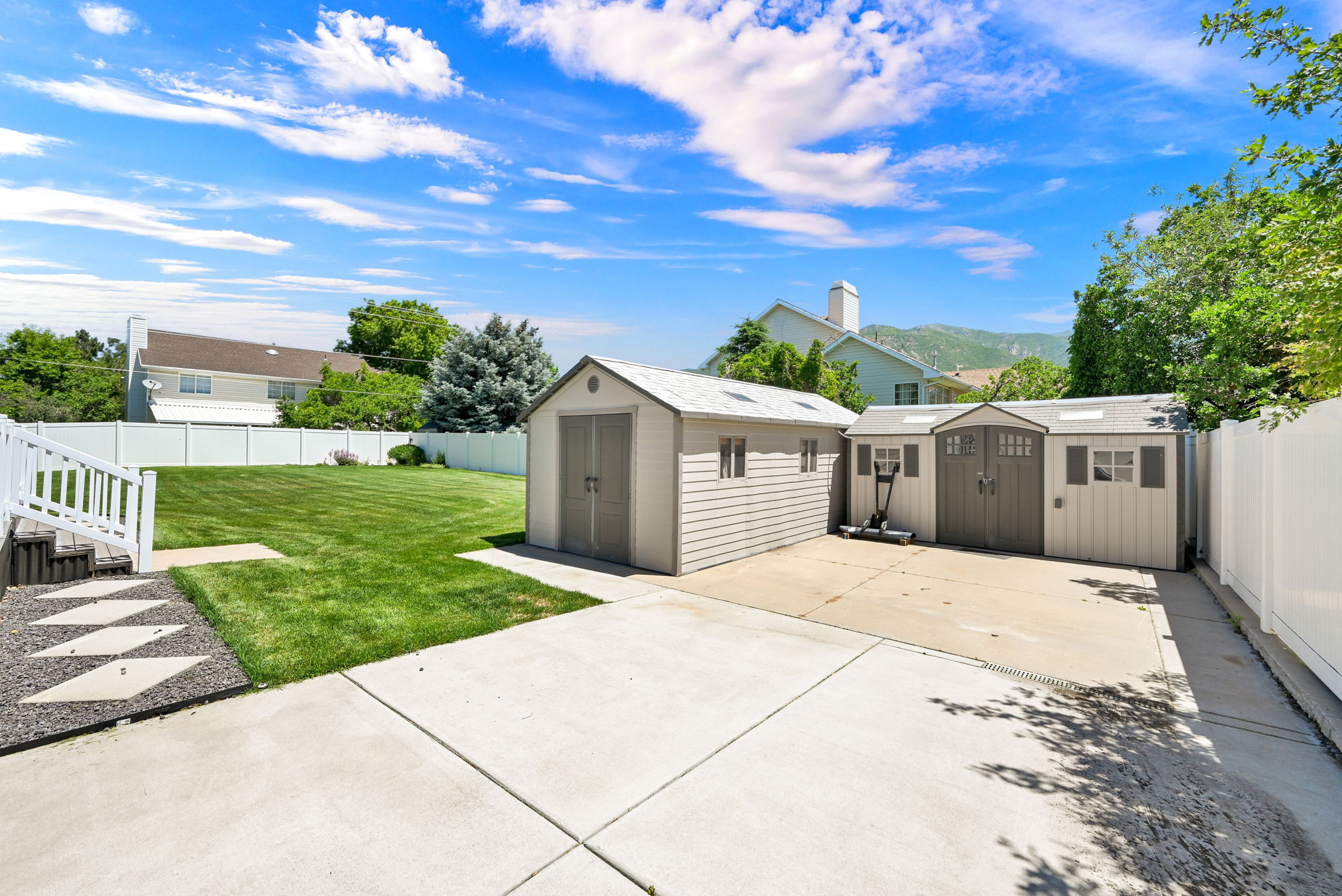 Expansive concrete patio area with two storage sheds featuring electricity in both sheds with double doors and side windows