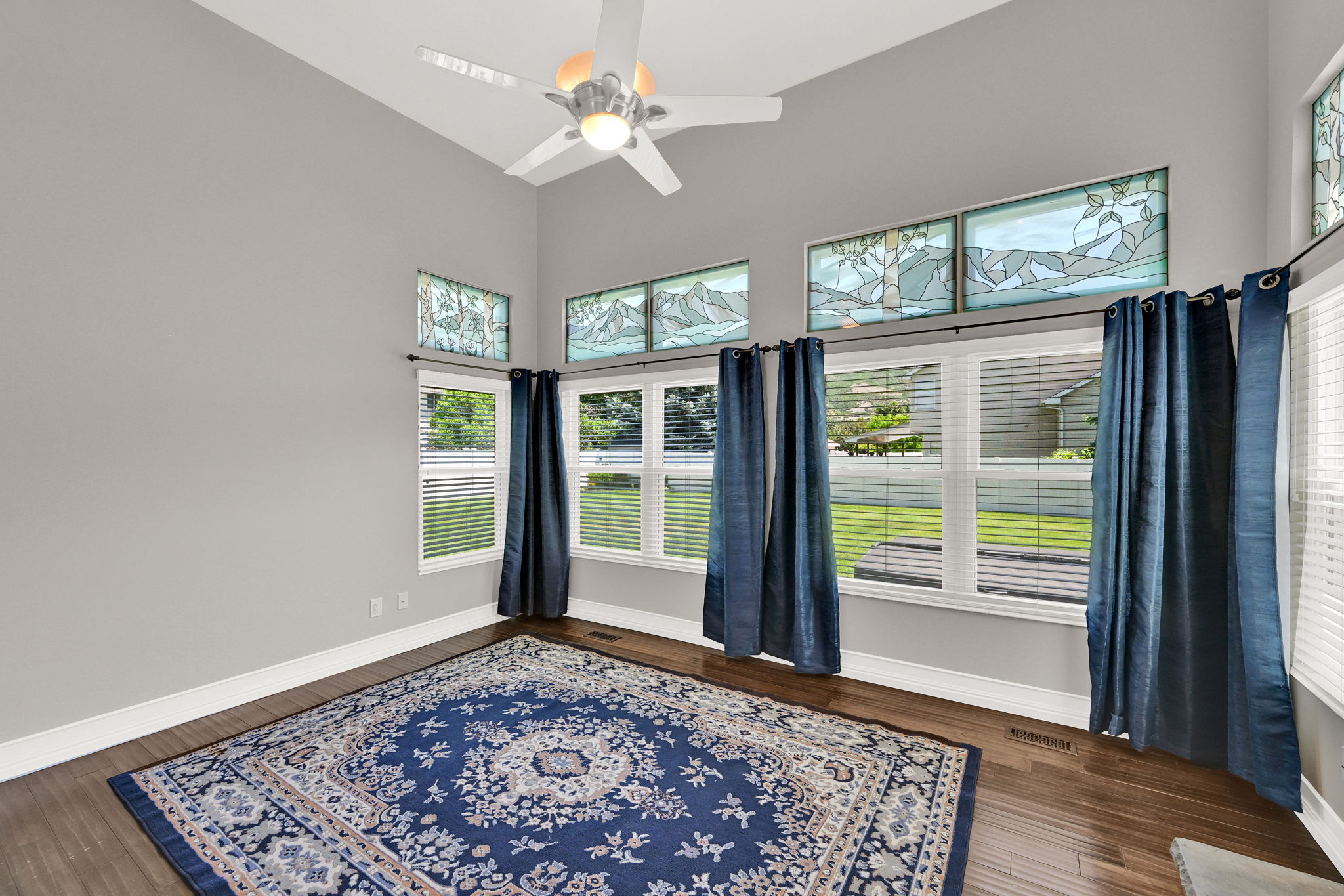 Vaulted ceiling with a ceiling fan and recessed lighting, wood-finish flooring, and multiple windows with stained glass transoms