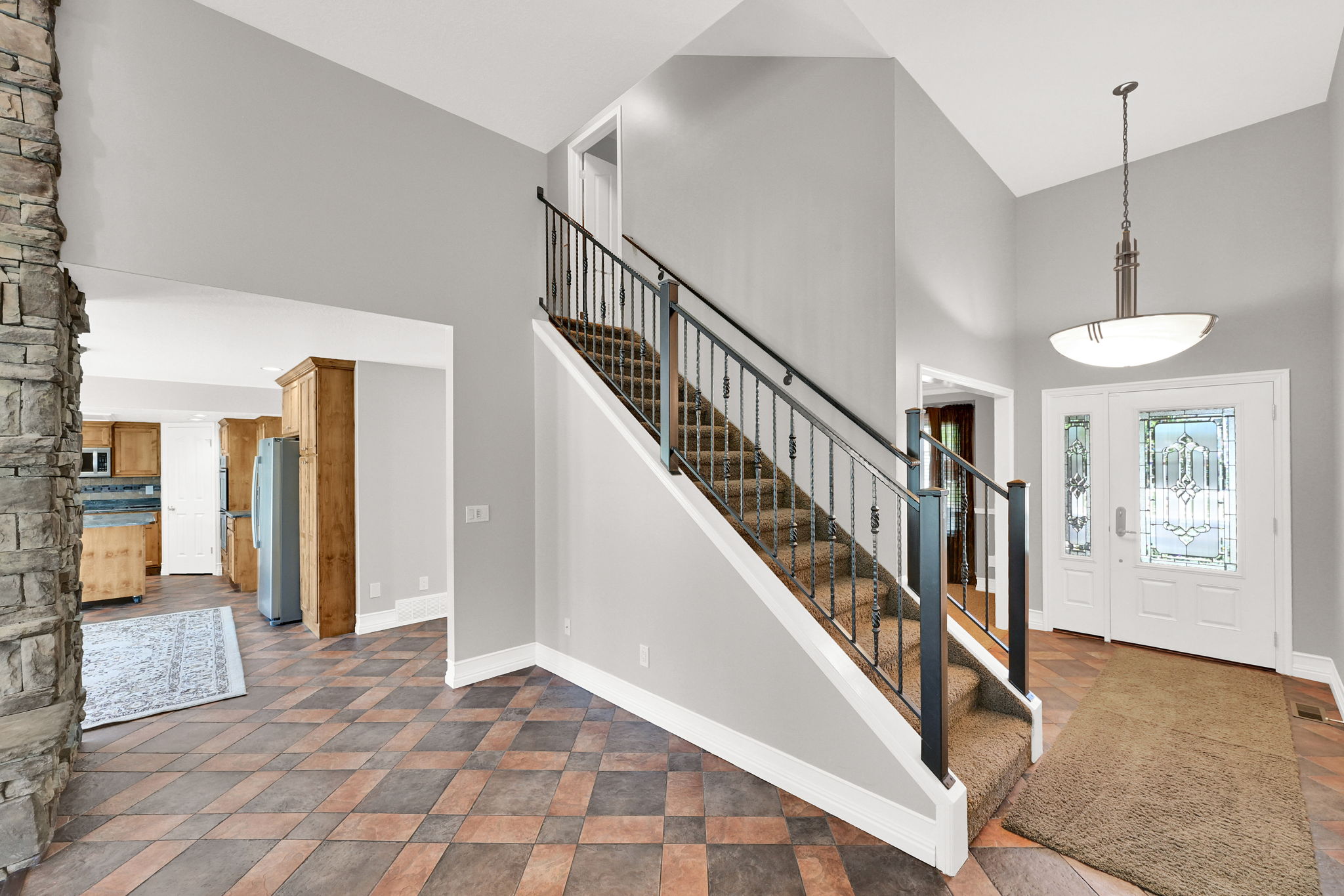 Two-story foyer featuring an ornate entry door with decorative glass, a staircase with wrought iron balusters, a stone fireplace, and patterned floor tiling