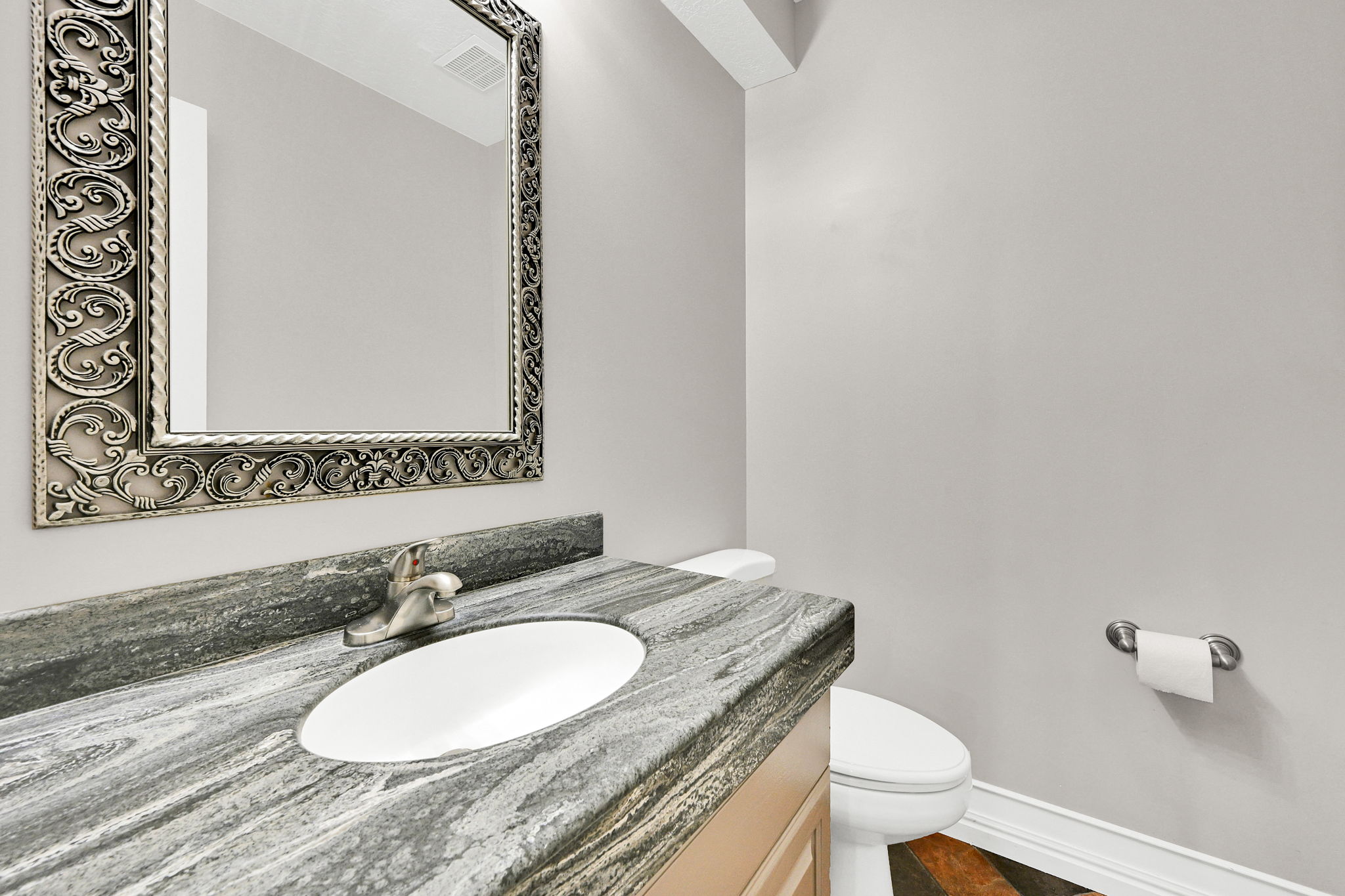 Main floor 1/2 bath with vanity featuring a patterned stone countertop with an integrated oval sink and brushed nickel faucet