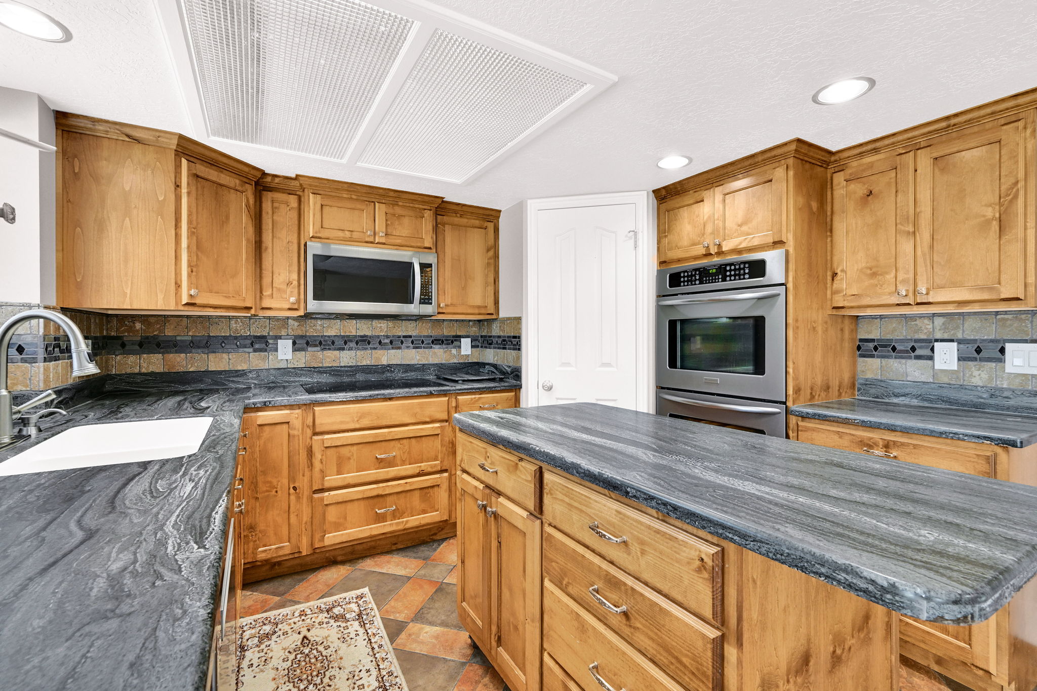 Kitchen featuring a large island with stone countertops, wood cabinetry, stainless steel appliances, and a tiled backsplash with electric or gas range top