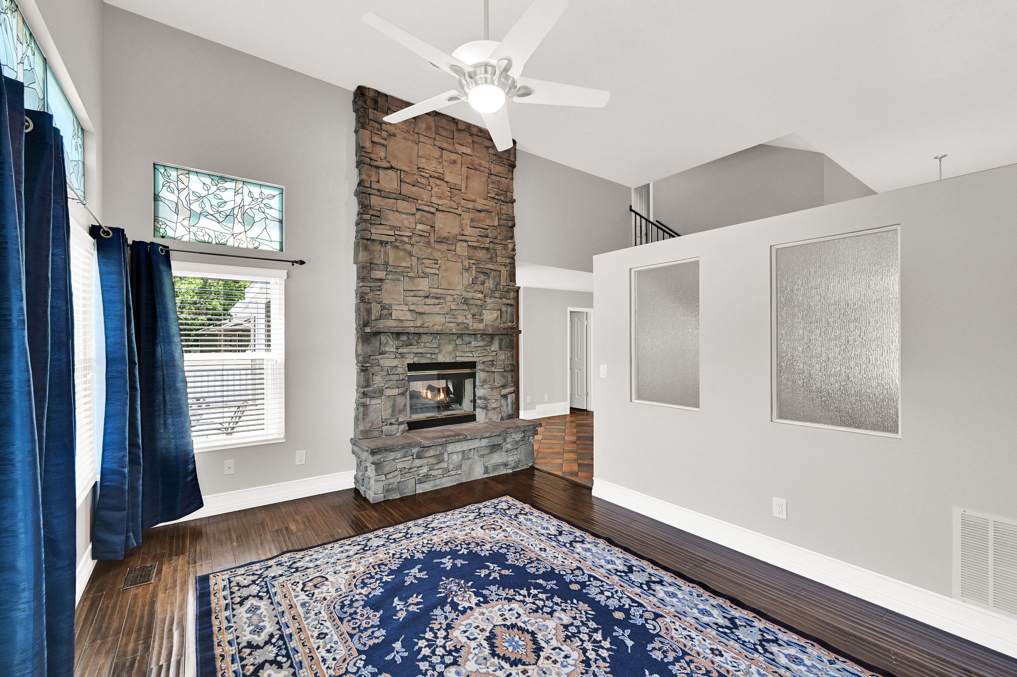 Stone-clad fireplace extending to the vaulted ceiling, complemented by wood-finish flooring and a ceiling fan