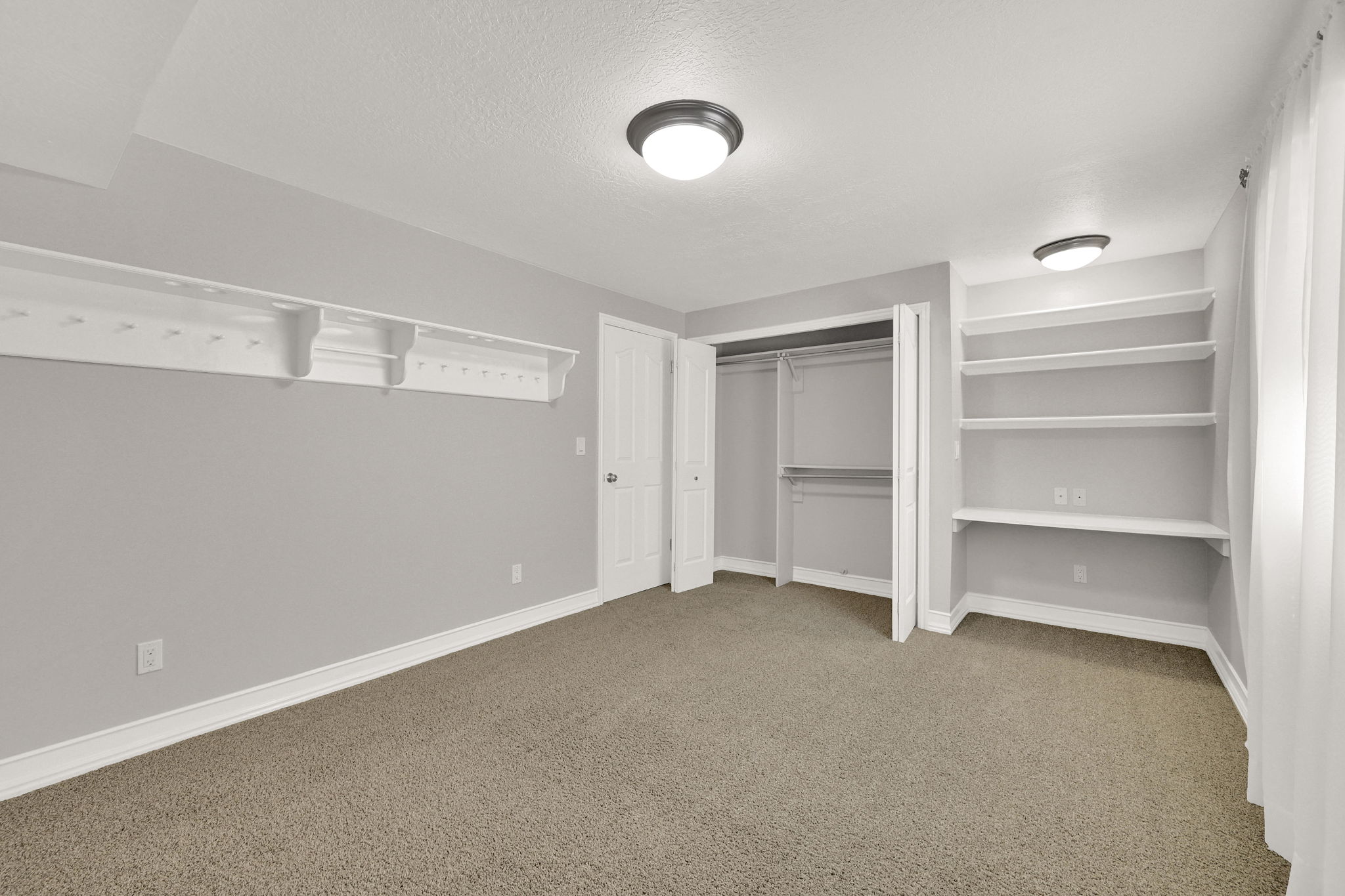 Bedroom #6 carpeted room featuring a built-in closet with bi-fold doors, white baseboards, built-in desk with shelves and a contemporary flush-mount ceiling light and large wall shelf with ball holders and hat posts built in