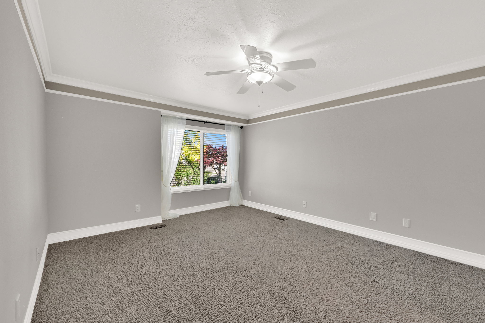 Primary suite bedroom with plush gray carpeting, light gray walls, and white crown molding with a fan/light