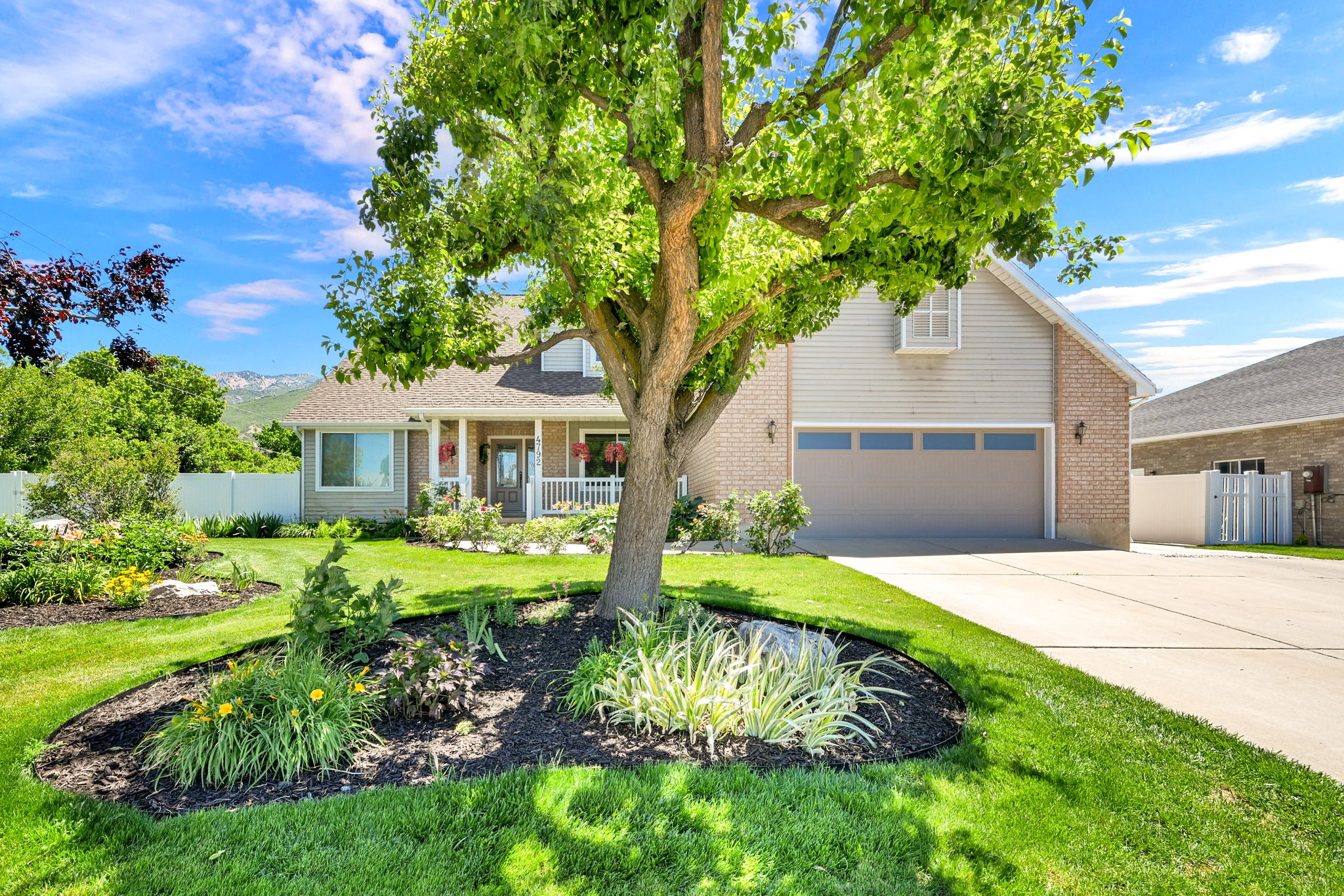 Expansive front yard featuring a mature shade tree, manicured lawn, and well-maintained garden beds