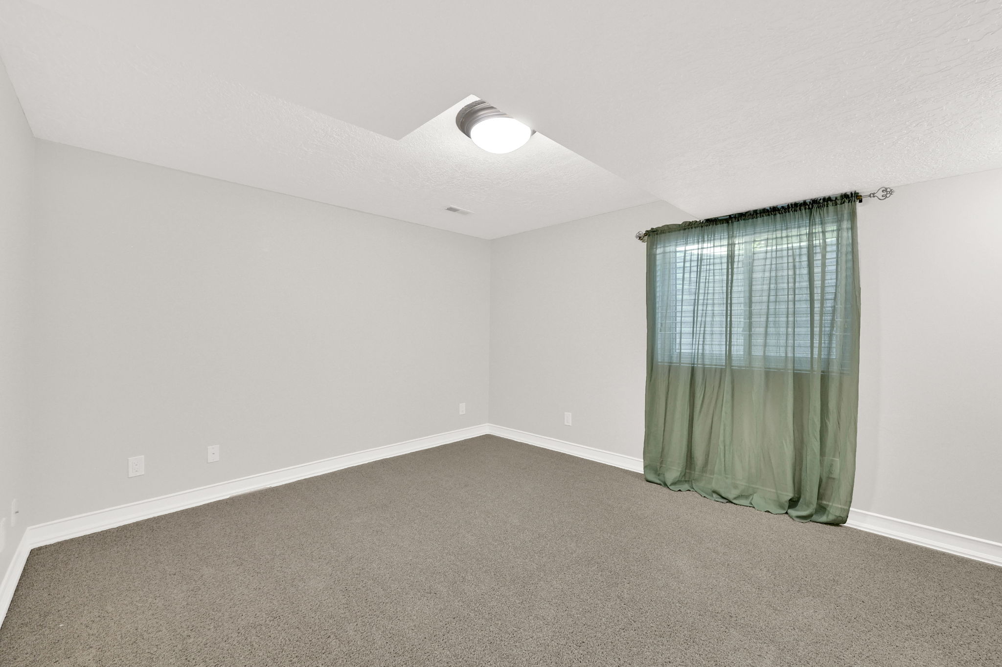 Bedroom #4 carpeted room with light grey walls, white baseboards, and a single window with a green sheer curtain