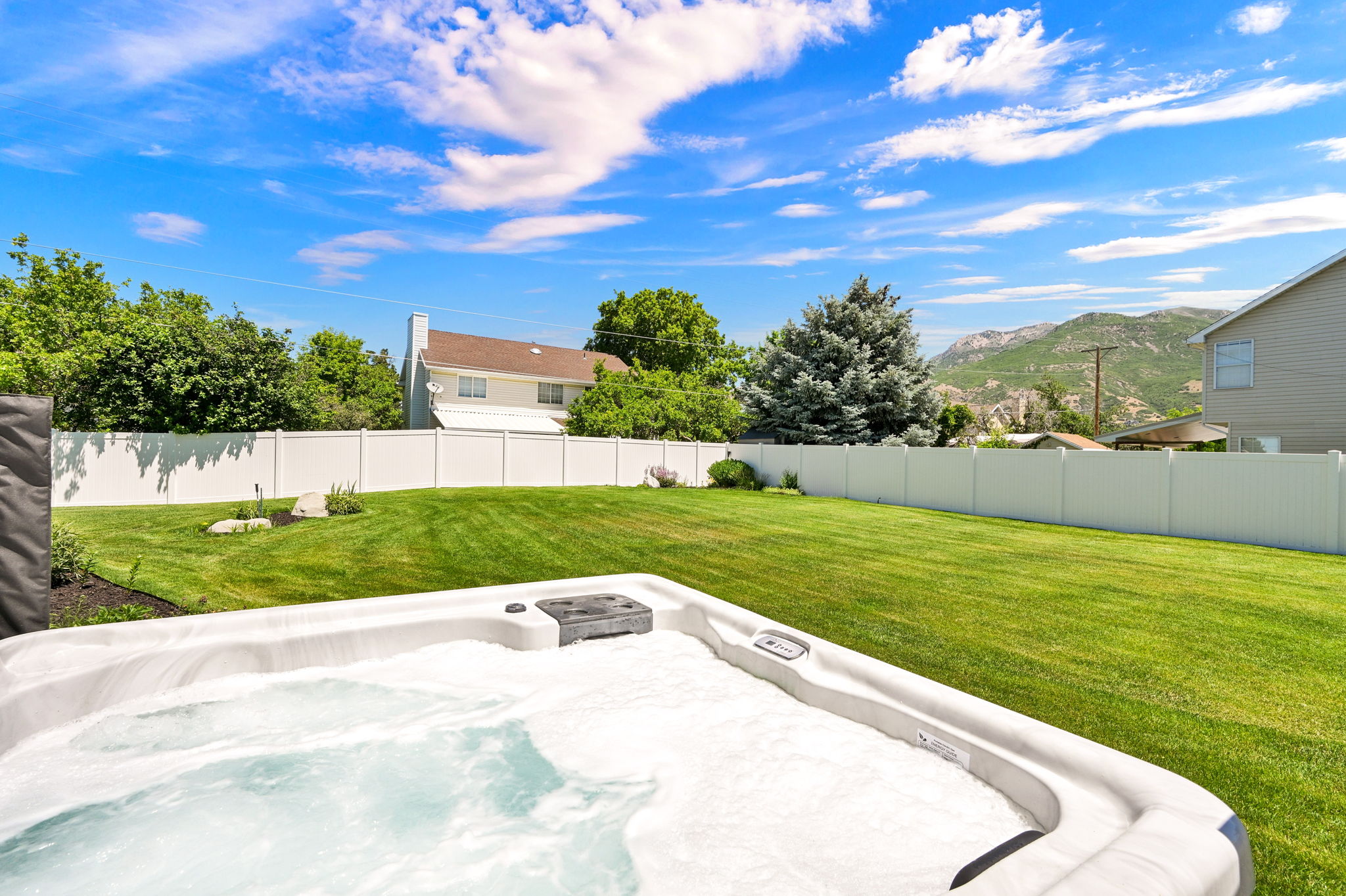Spacious backyard featuring a hot tub, manicured lawn, and white privacy fencing