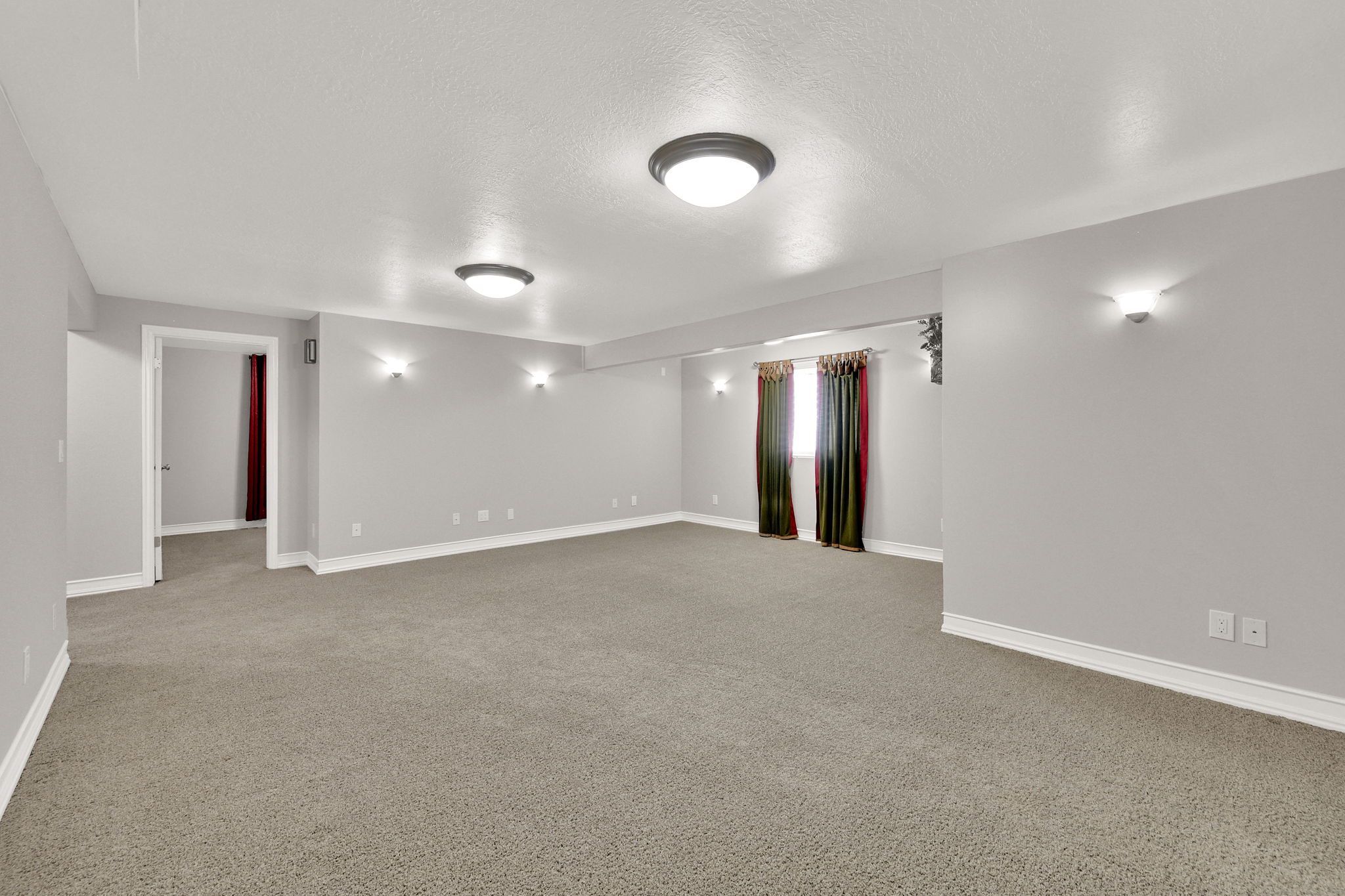 Spacious room featuring neutral carpeting, light gray walls, white baseboards, and ceiling-mounted flush lighting