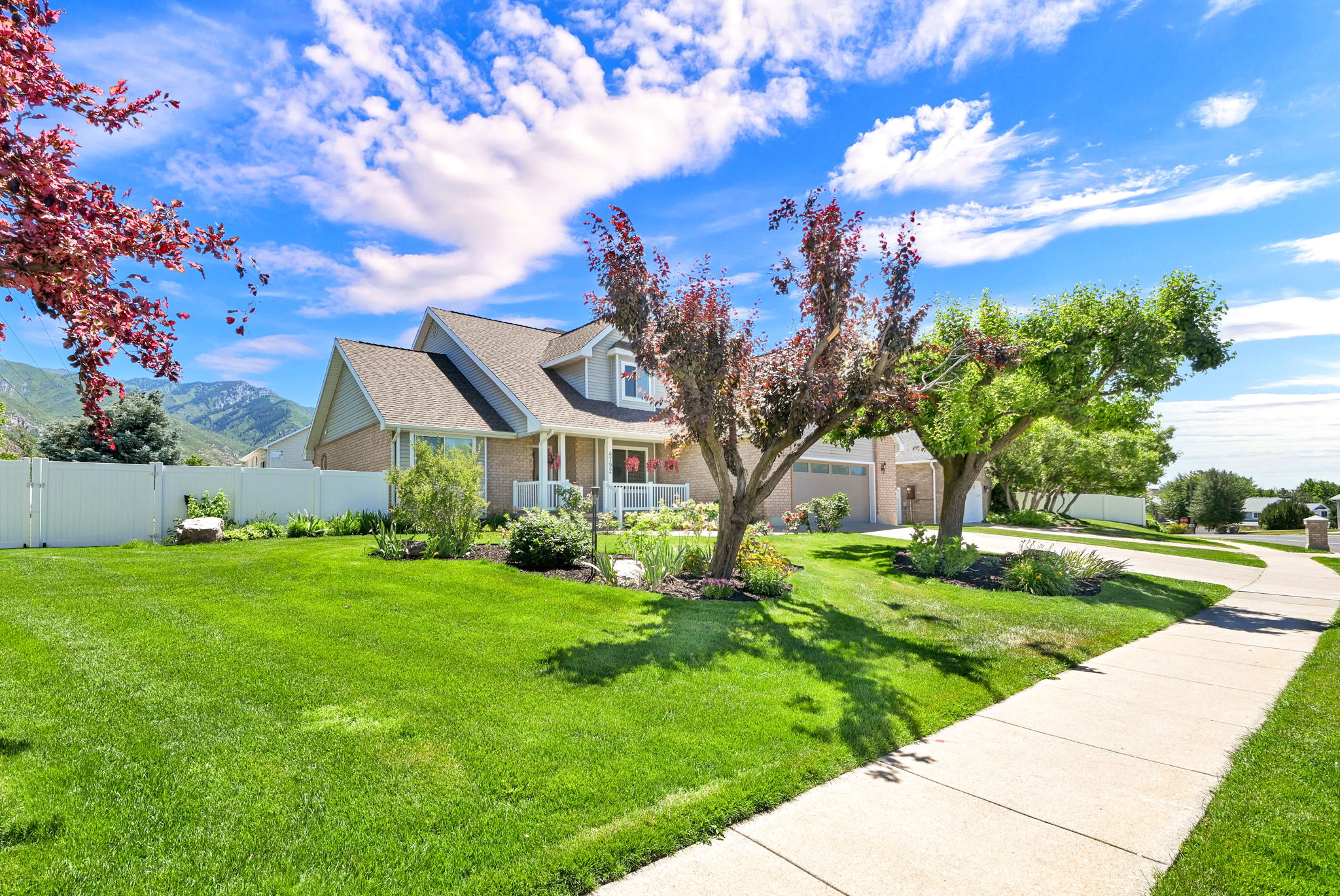 Traditional-style home featuring a brick and siding exterior, front porch with white vinyl wrapped columns, attached garage, mature landscaping, and a manicured lawn