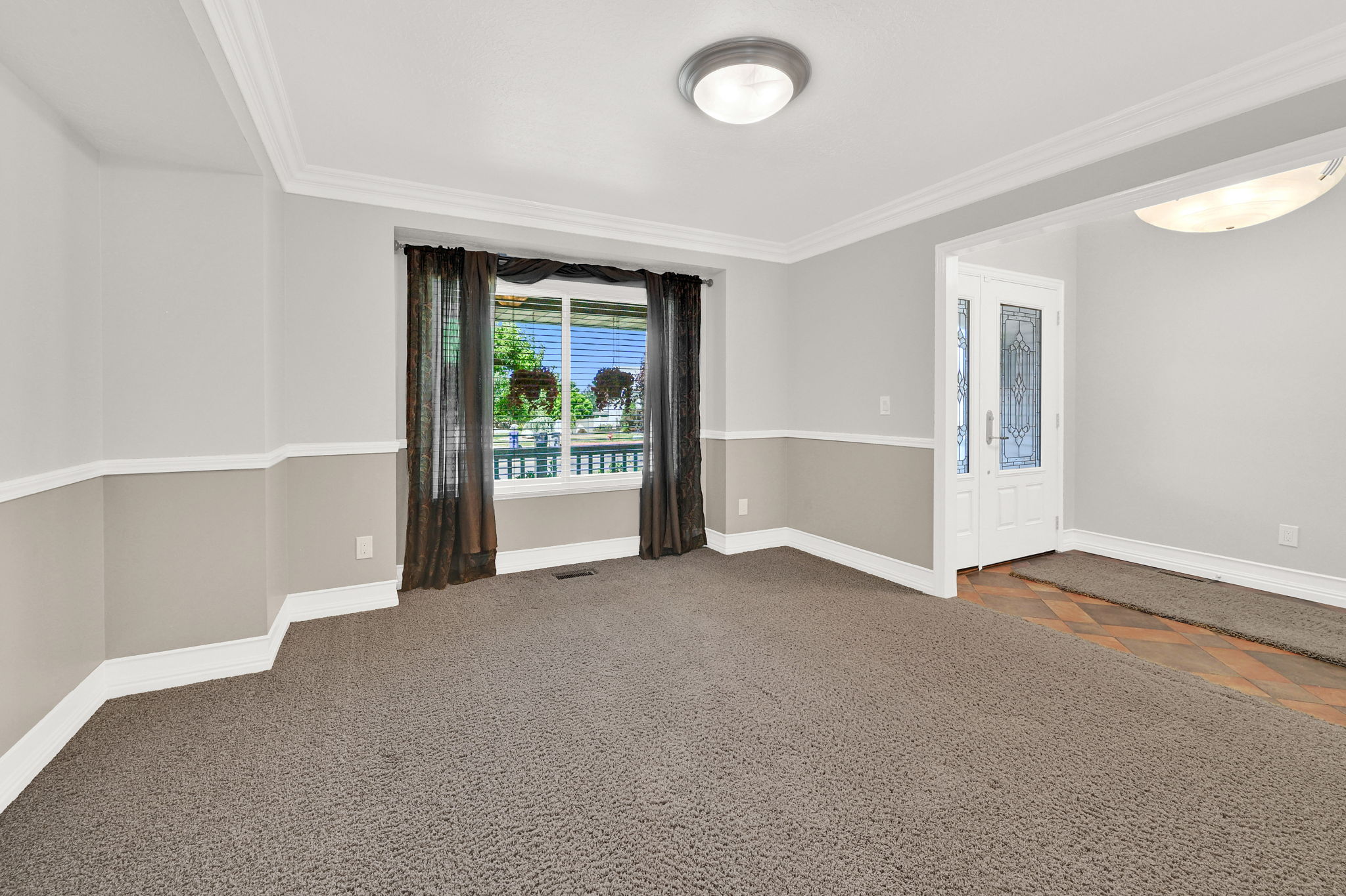 Interior space featuring two-tone wall paint, crown molding, and a large window with white trim just to the left of the front door