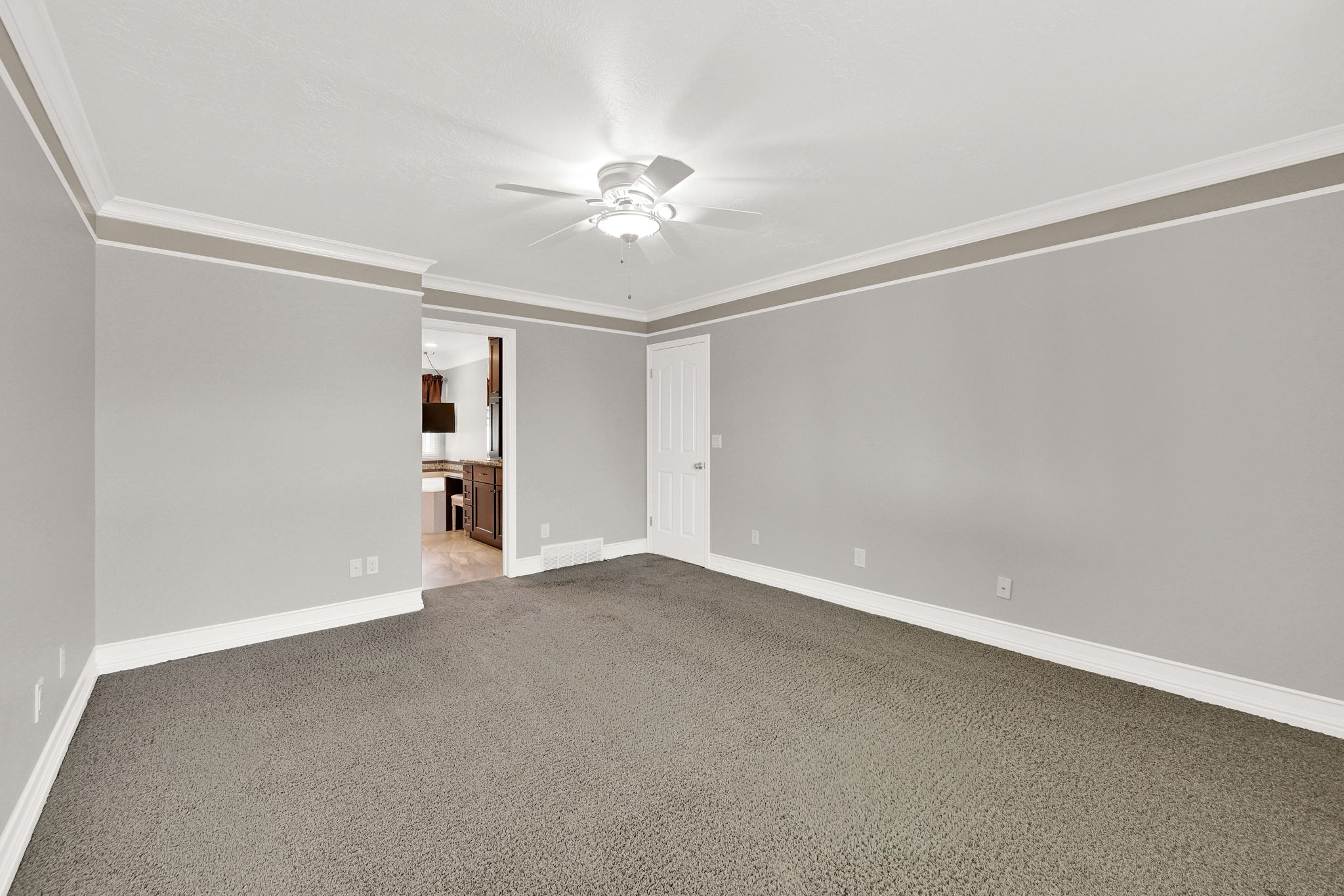 Spacious primary suite bedroom featuring neutral grey walls and contrasting white crown molding