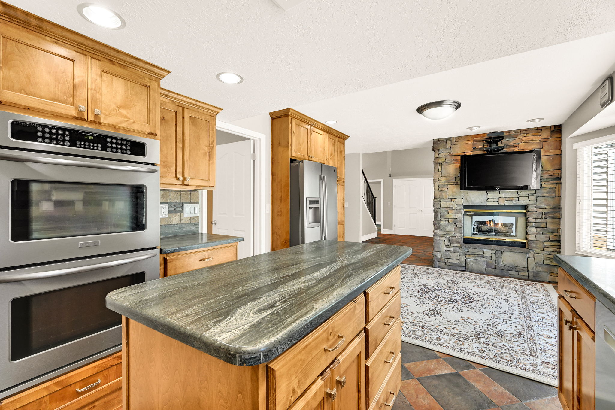 Kitchen island with a striated countertop, surrounded by wood cabinetry and with dual ovens
