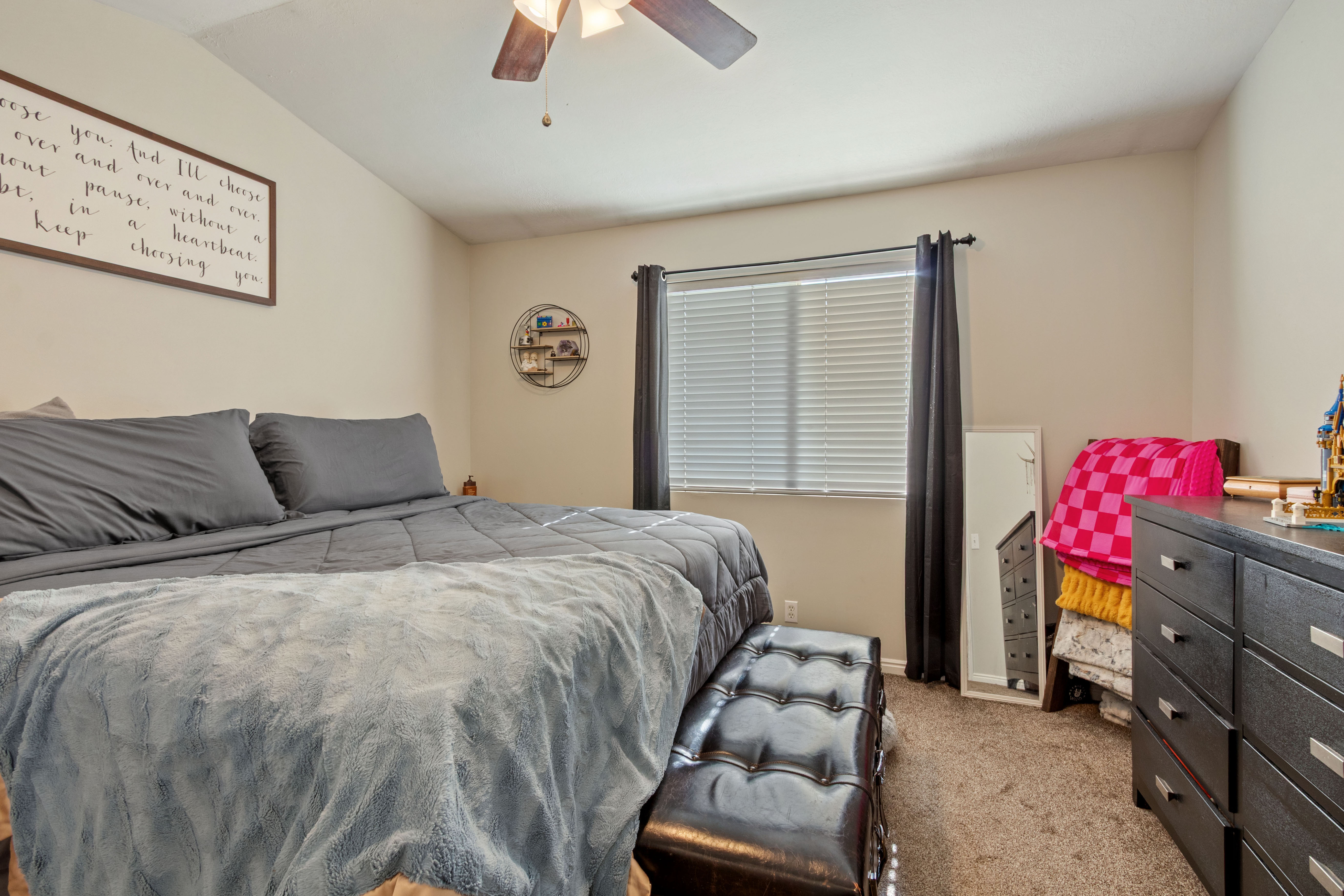 Spacious bedroom featuring neutral wall tones, textured carpet, and a ceiling fan with integrated lighting