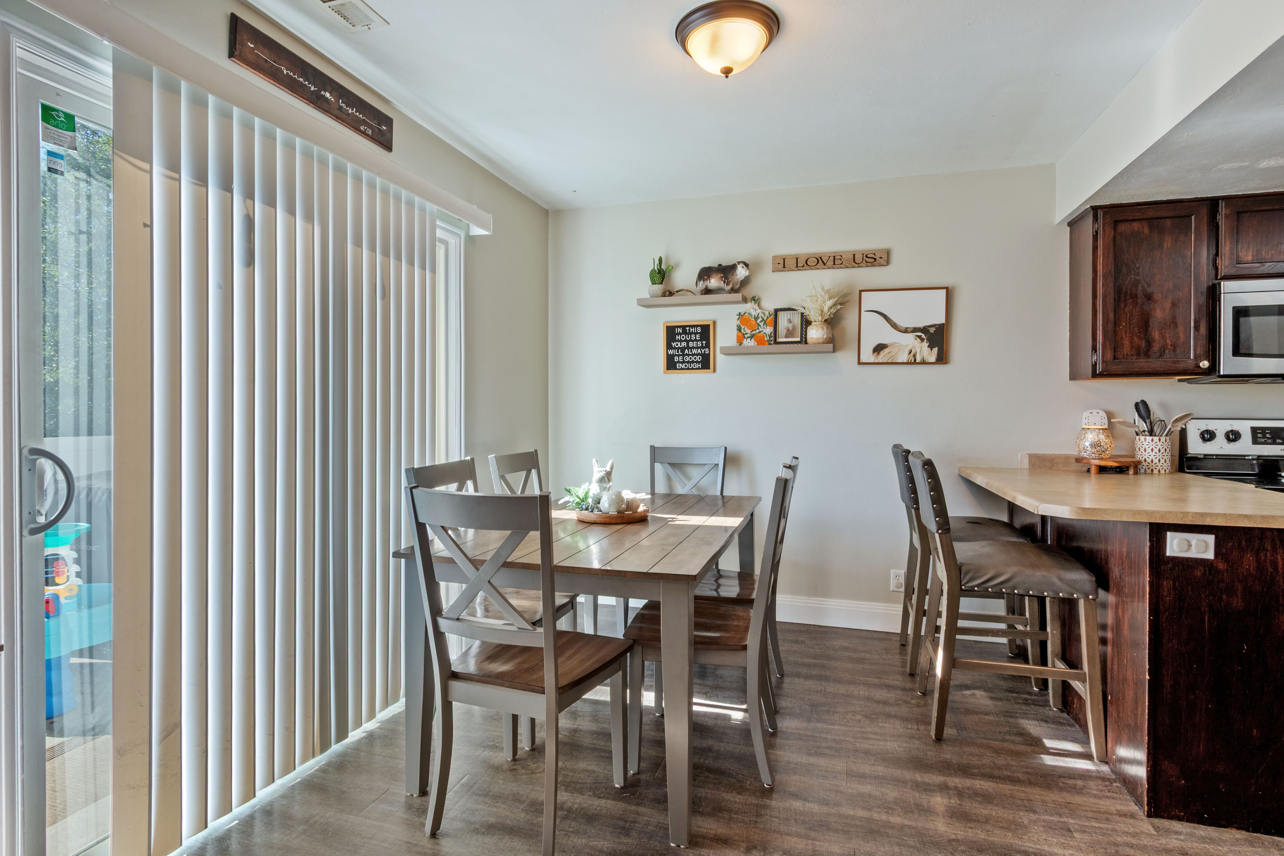 Dining area featuring wood-finish flooring, a sliding glass door with vertical blinds, and a kitchen pass-through with counter seating