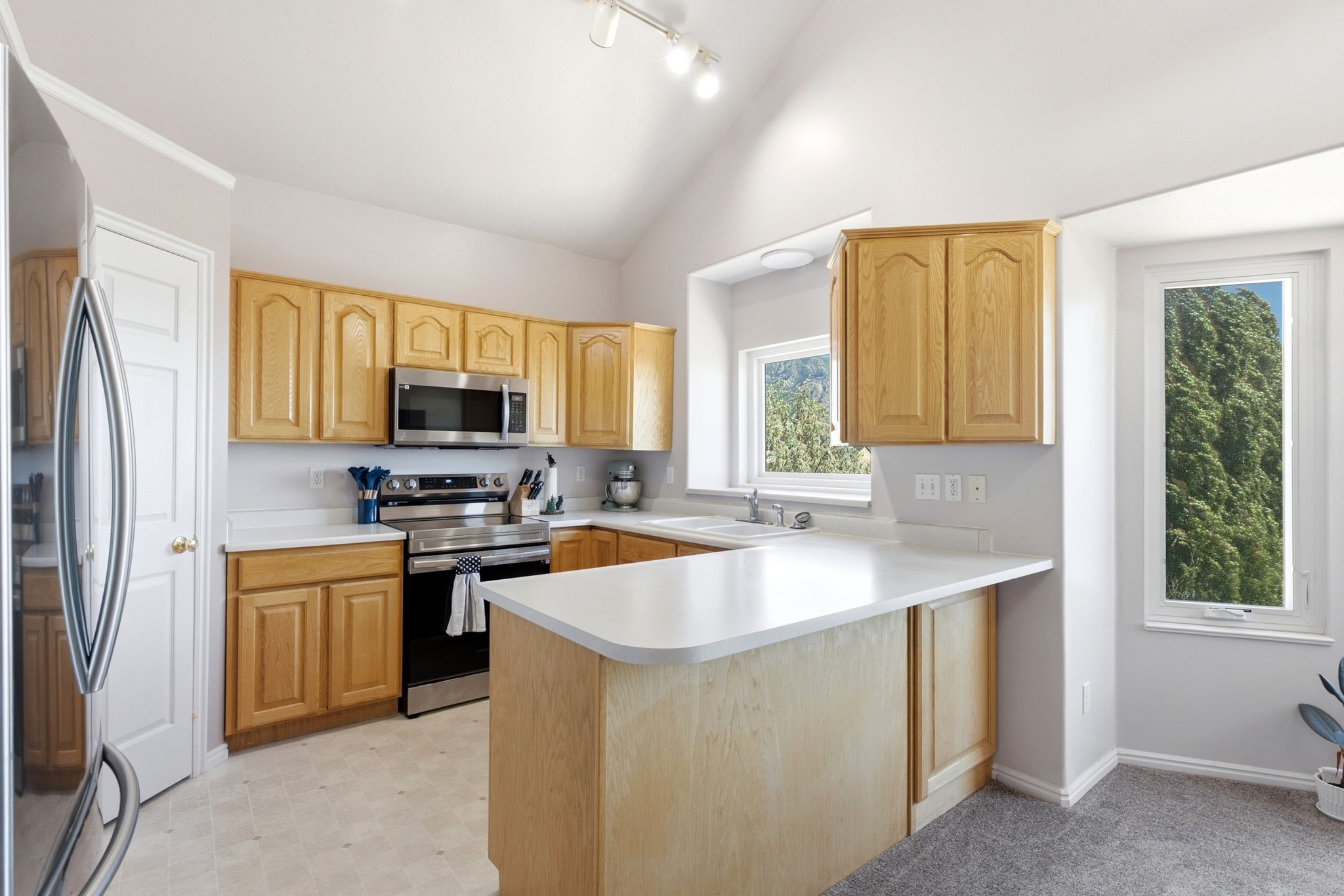 Kitchen featuring wood cabinetry, white countertops, stainless steel appliances, and a vaulted ceiling with track lighting