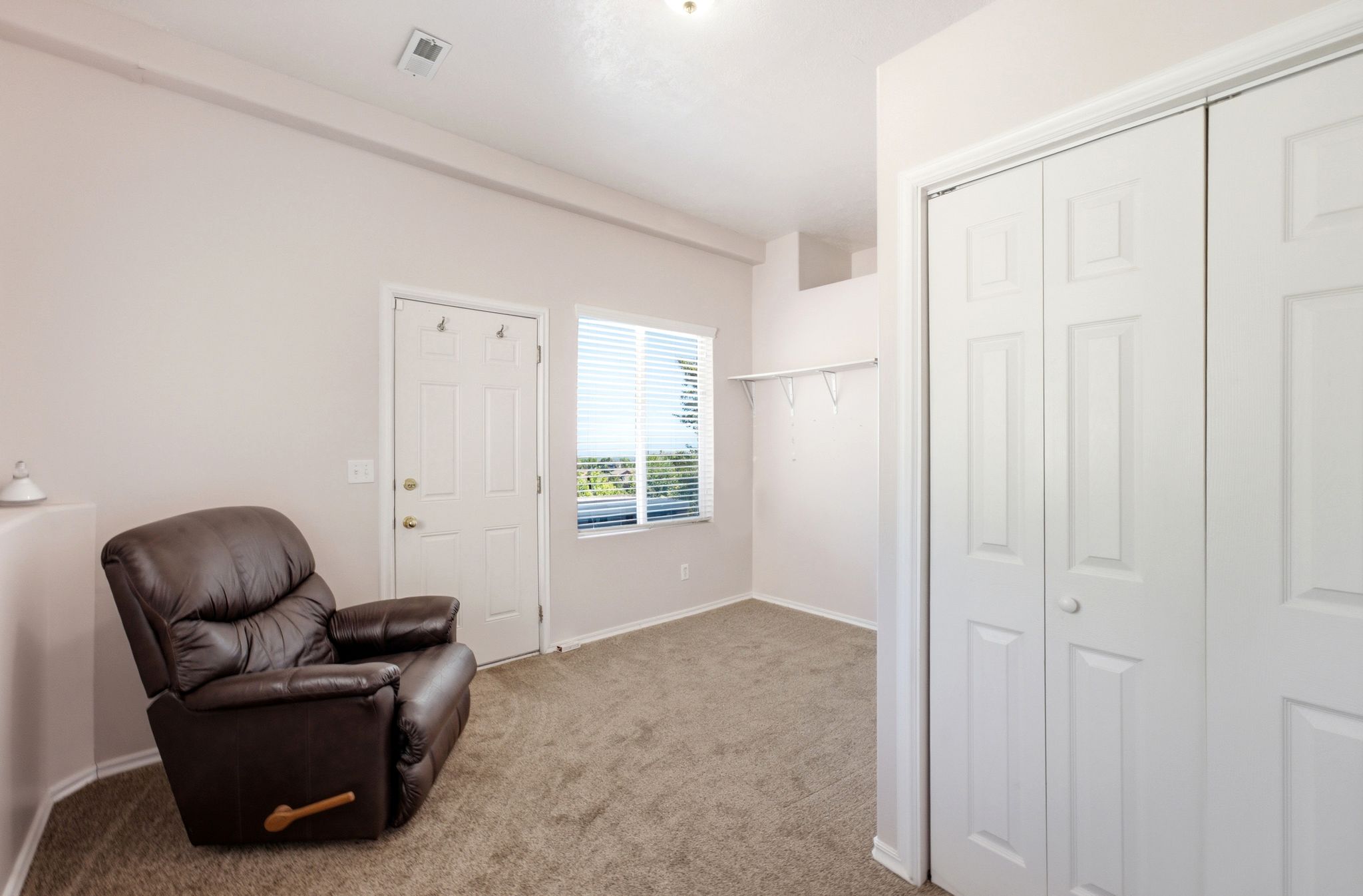 Spacious room featuring neutral carpeting, a white paneled door, and a window with horizontal blinds
