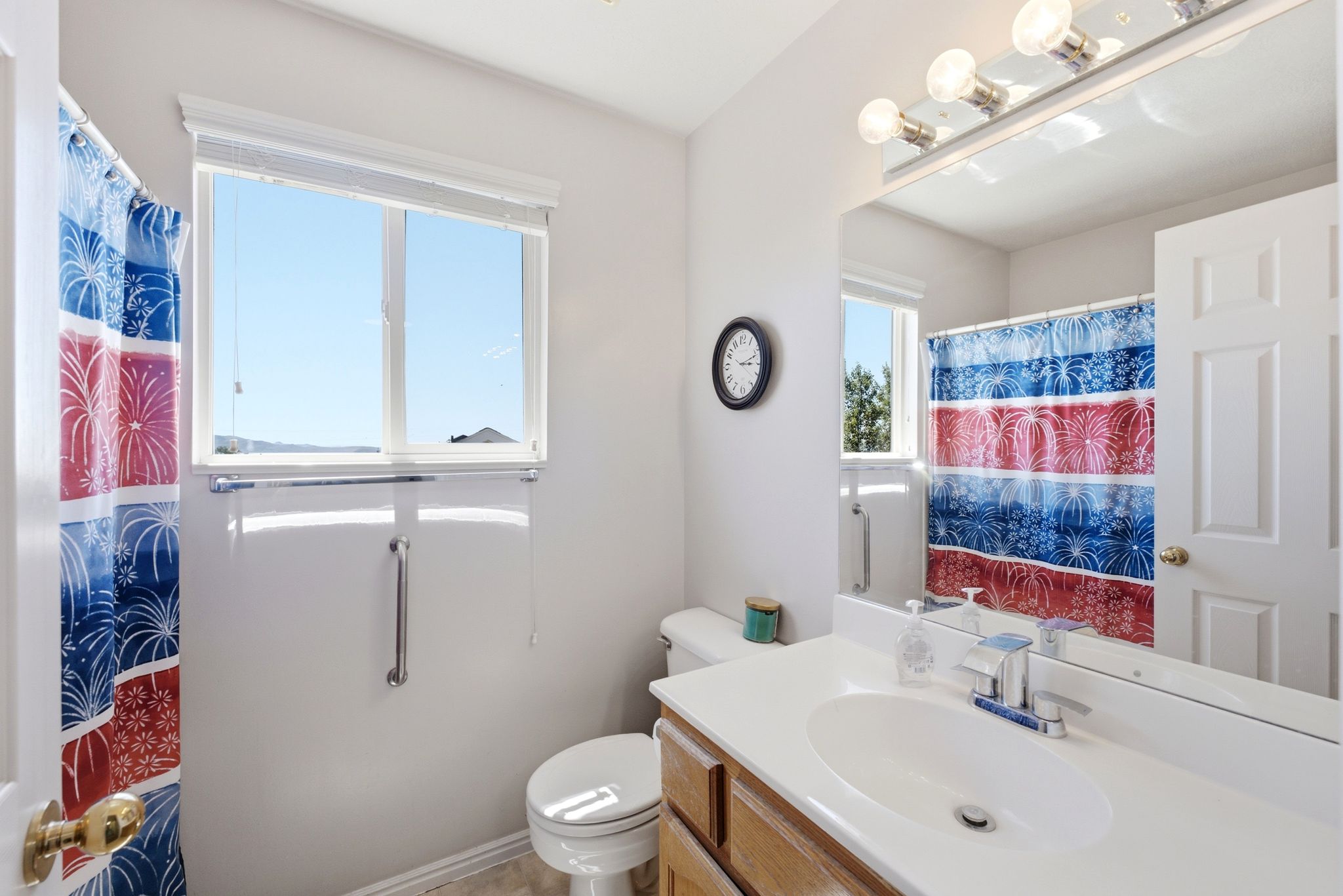 Bathroom featuring a window with privacy blinds, a toilet, a vanity with an integrated sink, and a large mirror with overhead lighting